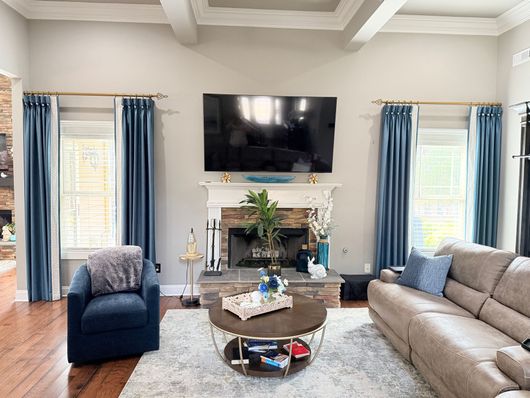 Living room with gray sofa, blue chair, wall-mounted TV, and fireplace beneath a coffered ceiling