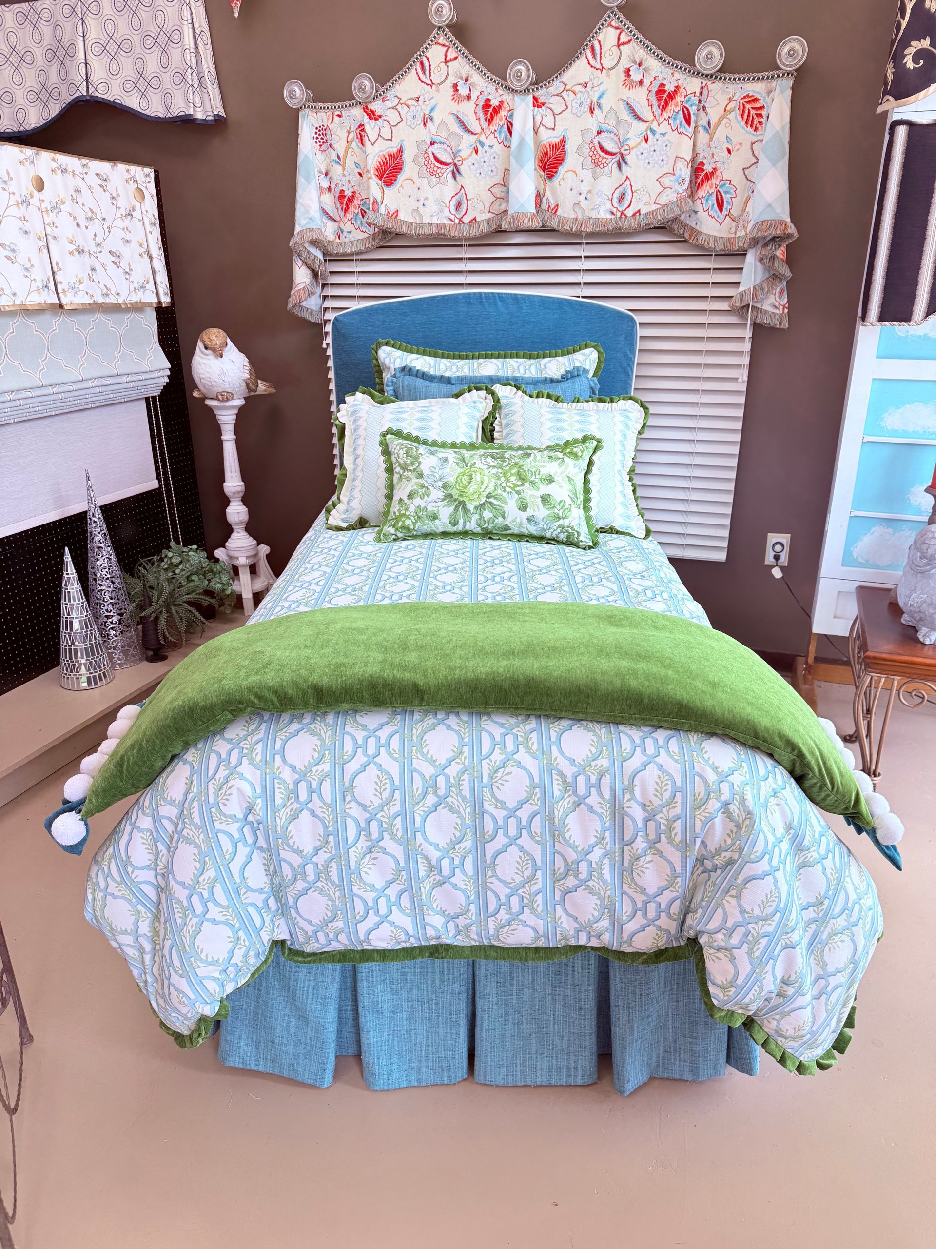 Decorated bed with floral bedding, green throw, and blue skirt in a cozy bedroom display