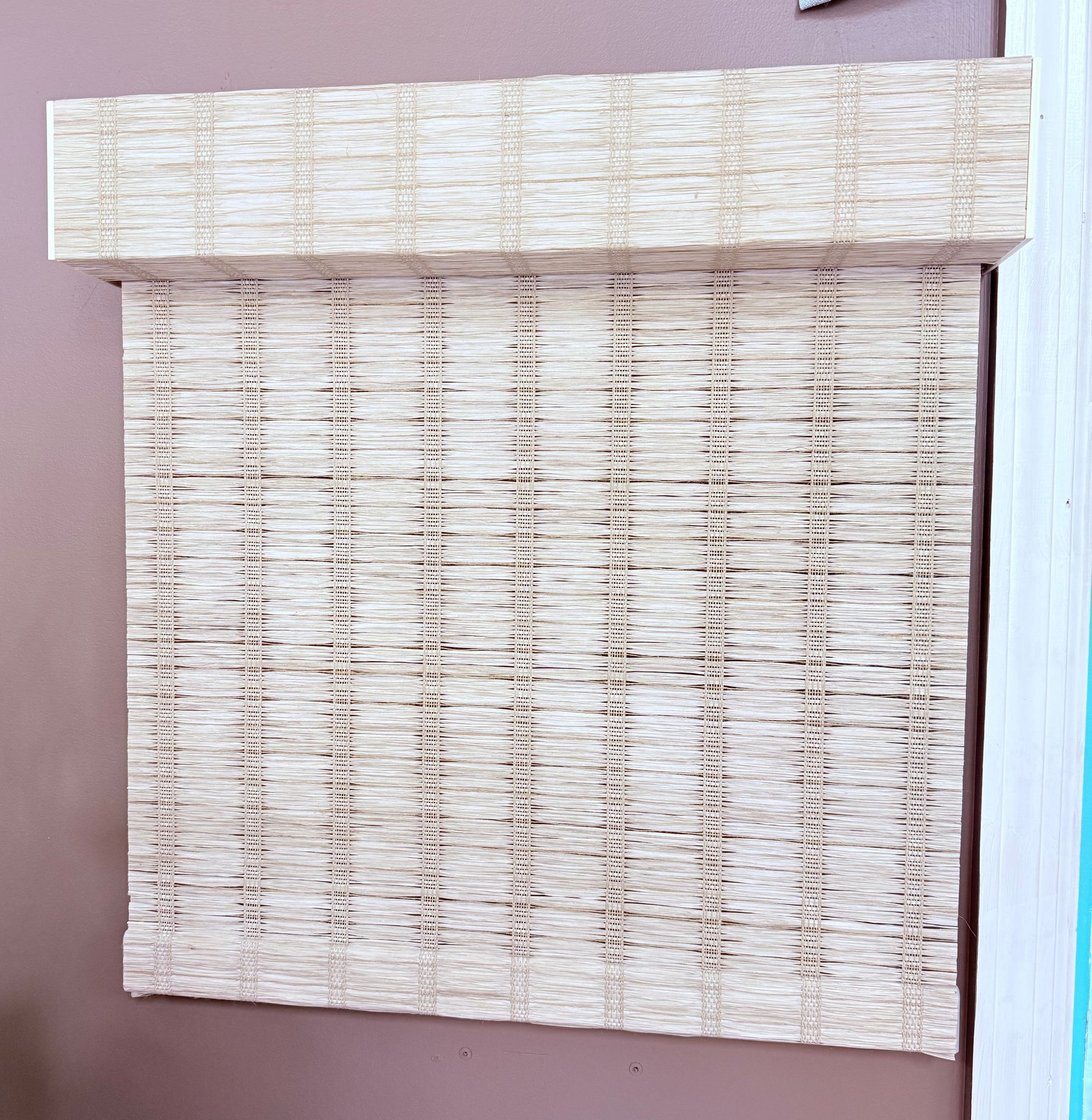 Closed woven bamboo window blind against a mauve wall