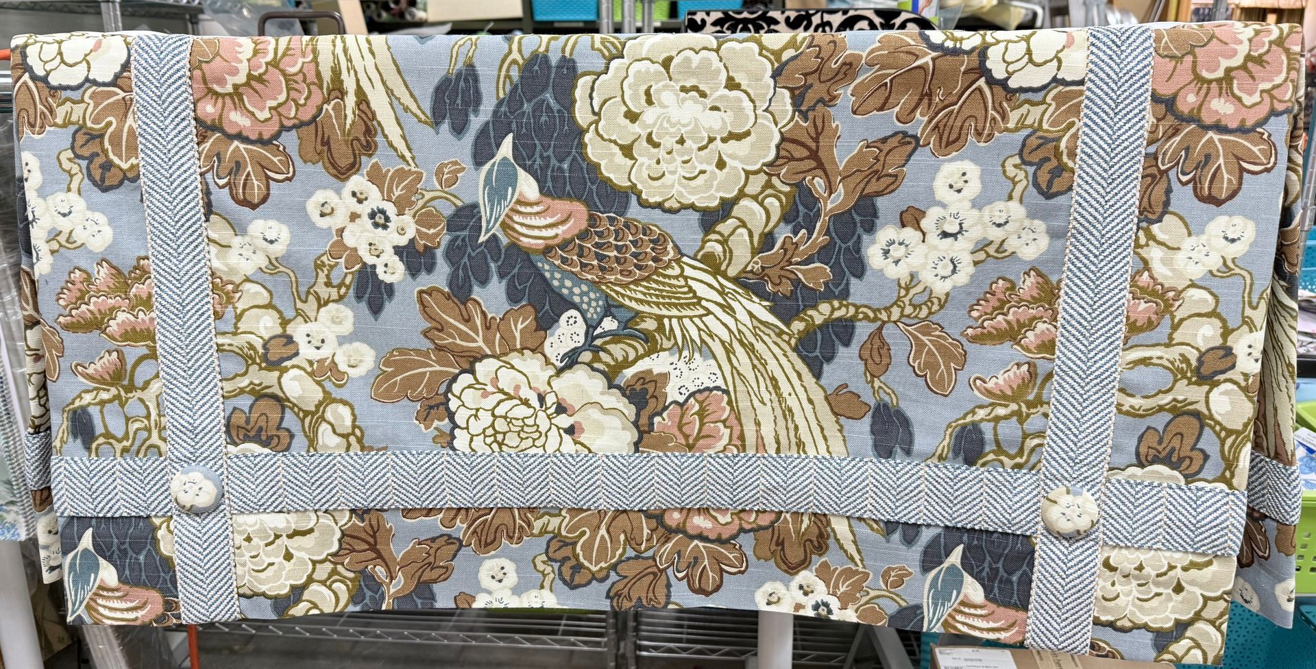 Floral patterned fabric cover with beige straps and metal rings on a cart or bag.