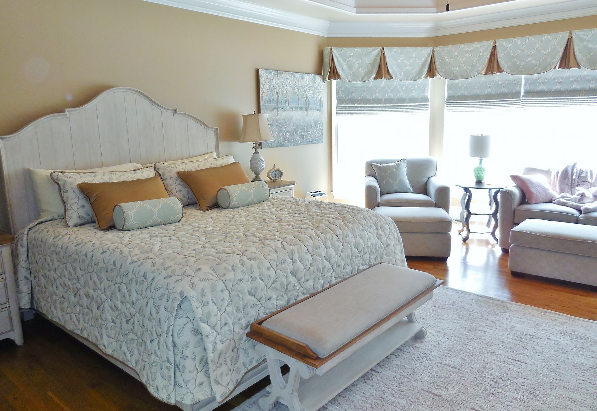 Bright bedroom with a large bed, ottoman bench, and sitting area by a window