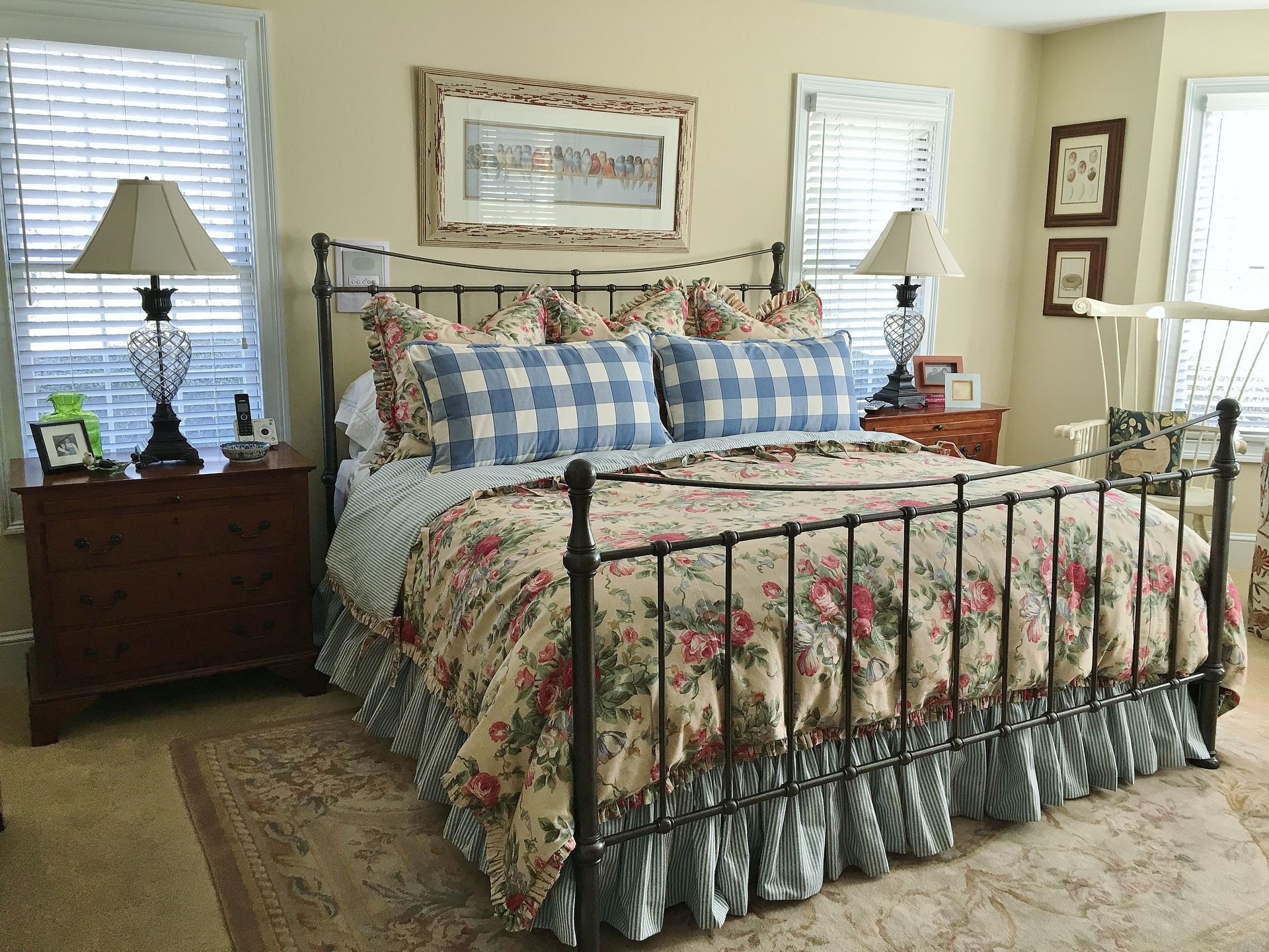 Cozy floral bedroom with iron bed, blue plaid pillows, nightstands, lamps, and framed wall art