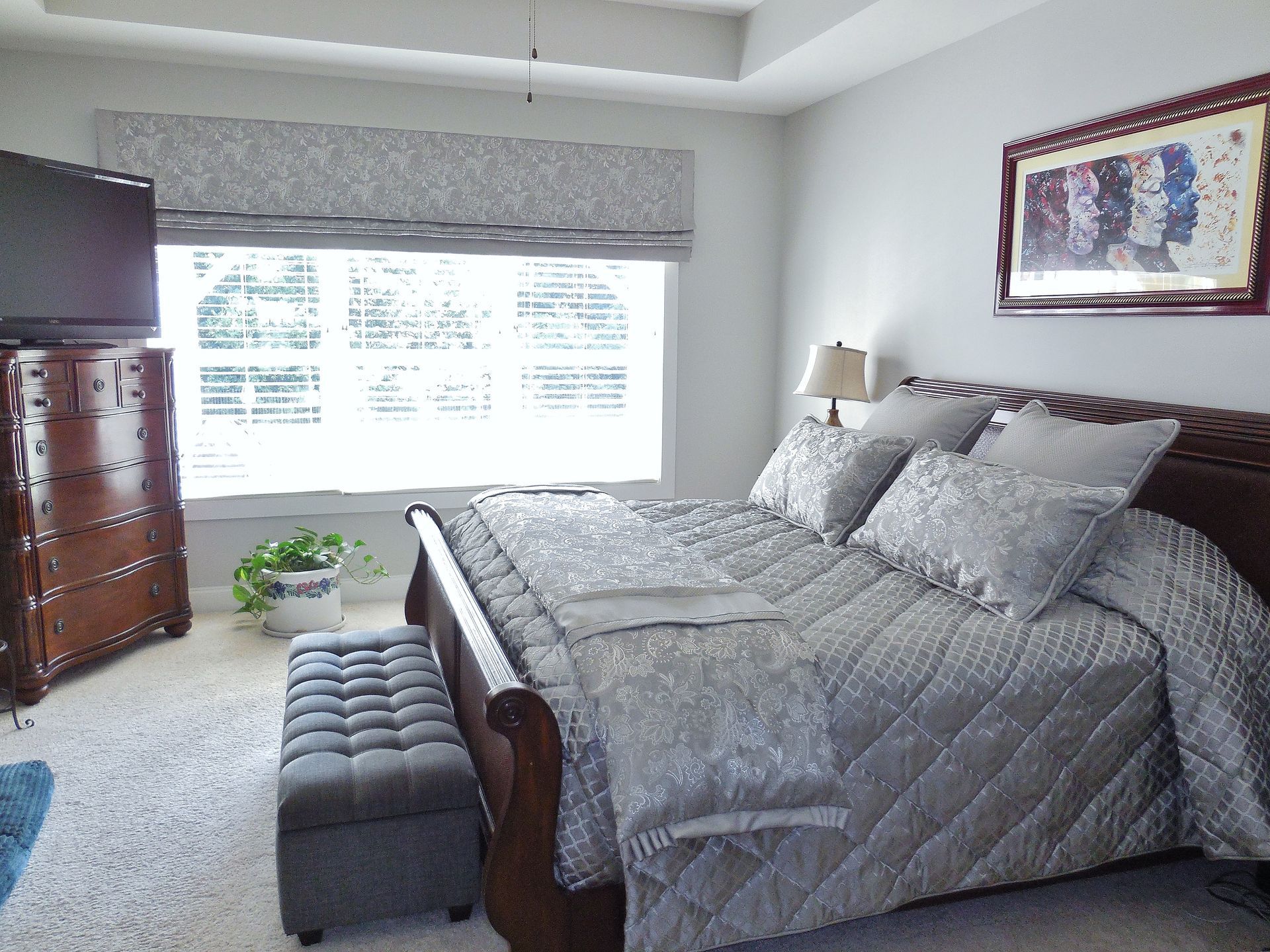Bright bedroom with a gray bed, window seat, dresser, and framed wall art.