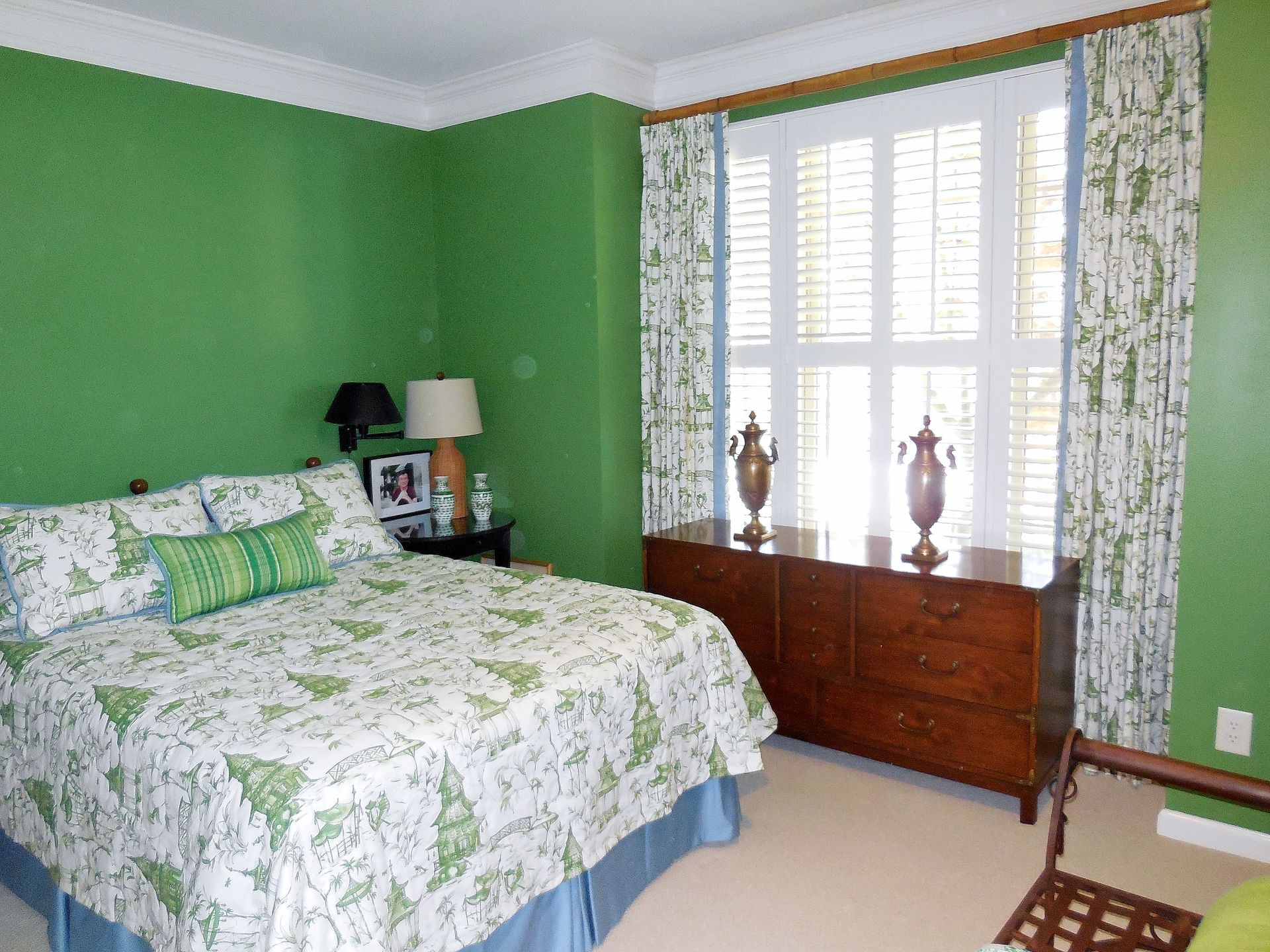 Green bedroom with floral bedspread, window, and wooden dresser