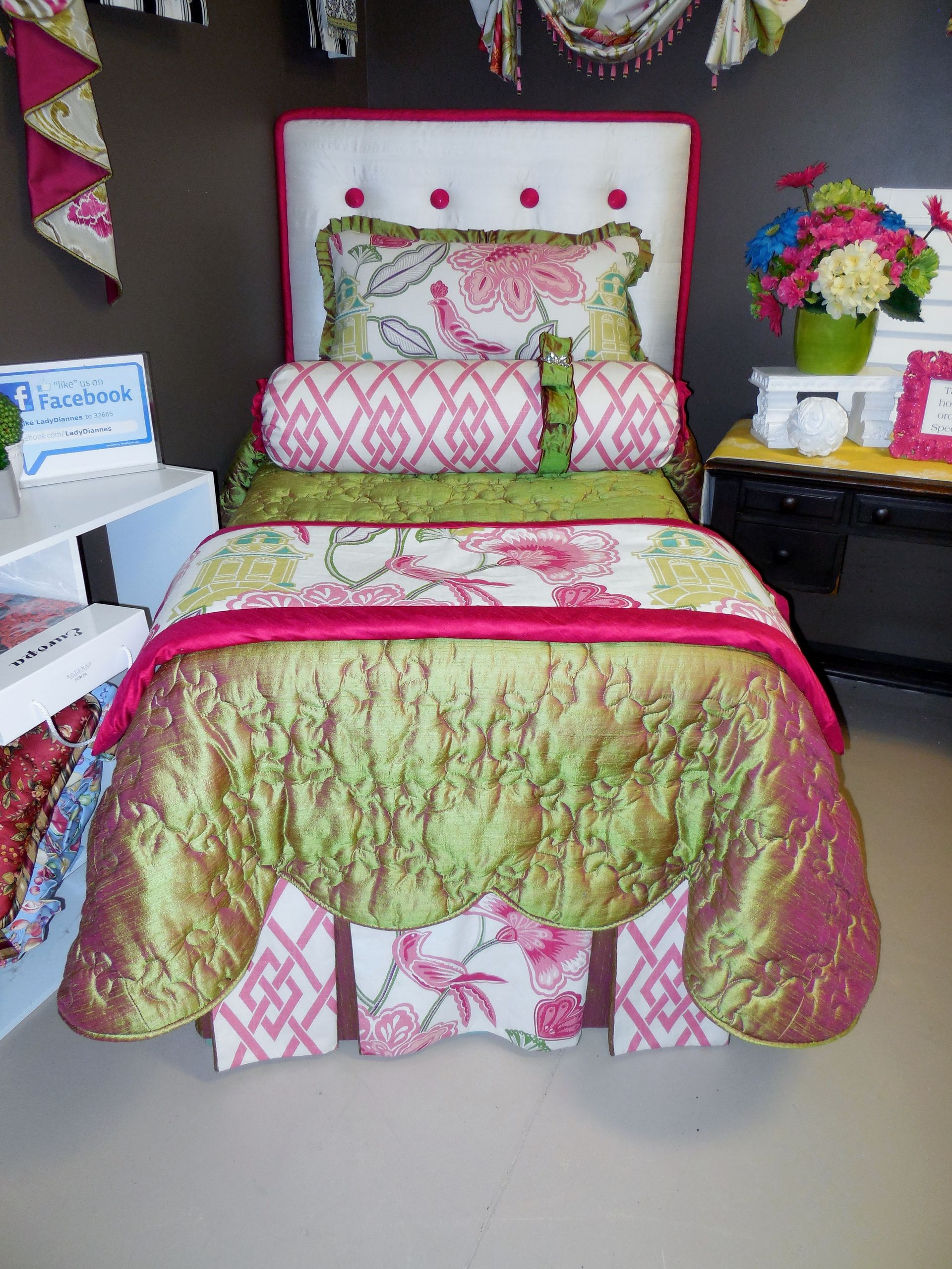 Colorful quilted bed with pink and green bedding, matching pillows, and floral decor in a bedroom display