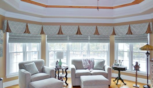 Bright sunroom with white armchairs, side tables, and tall windows with patterned valances