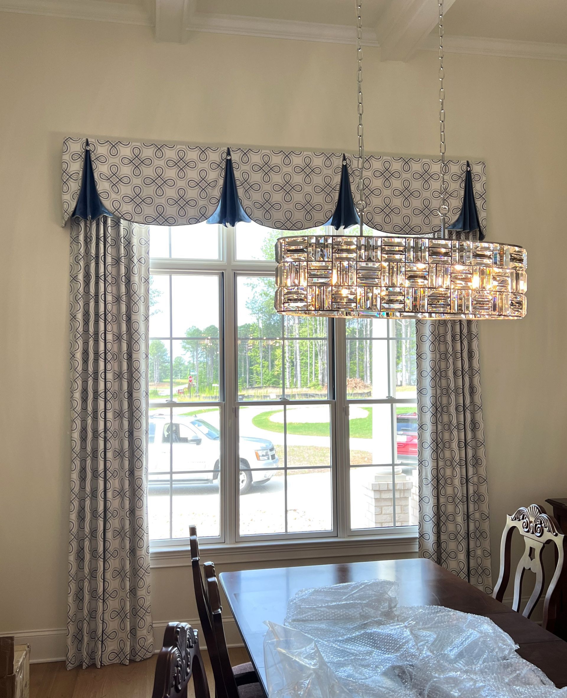 Dining room with a window, patterned curtains, and a glass chandelier over a table