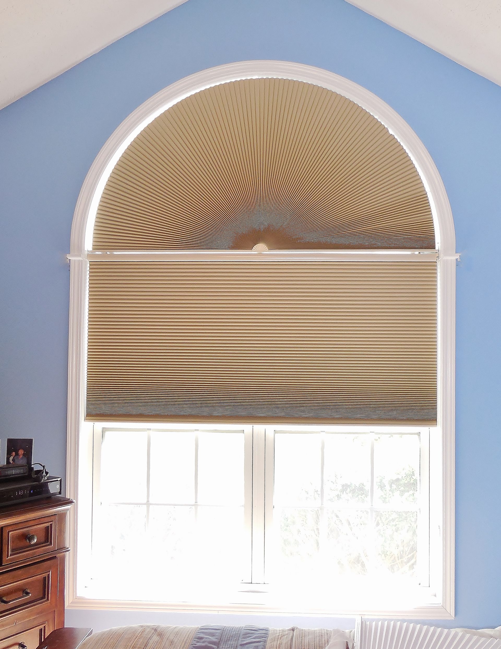 Blue room with arched window and woven Roman shade, sunlight streaming through a lower pane.