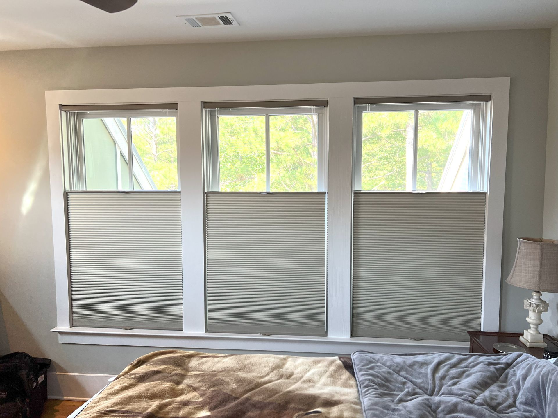 Bedroom with three windows covered by gray striped shades and bright daylight, above a bed with tan and gray blankets