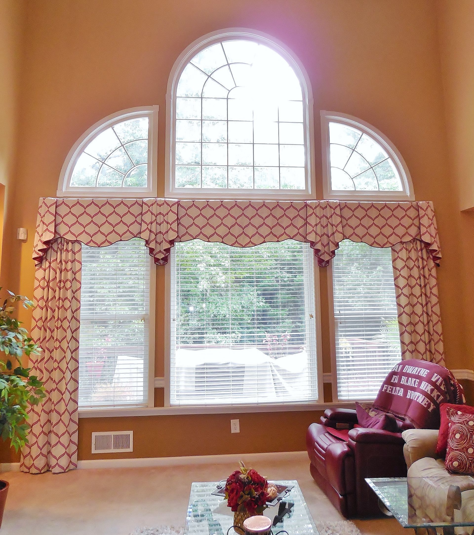 Living room with large arched windows, peach walls, red sofa, and a small floral table centerpiece
