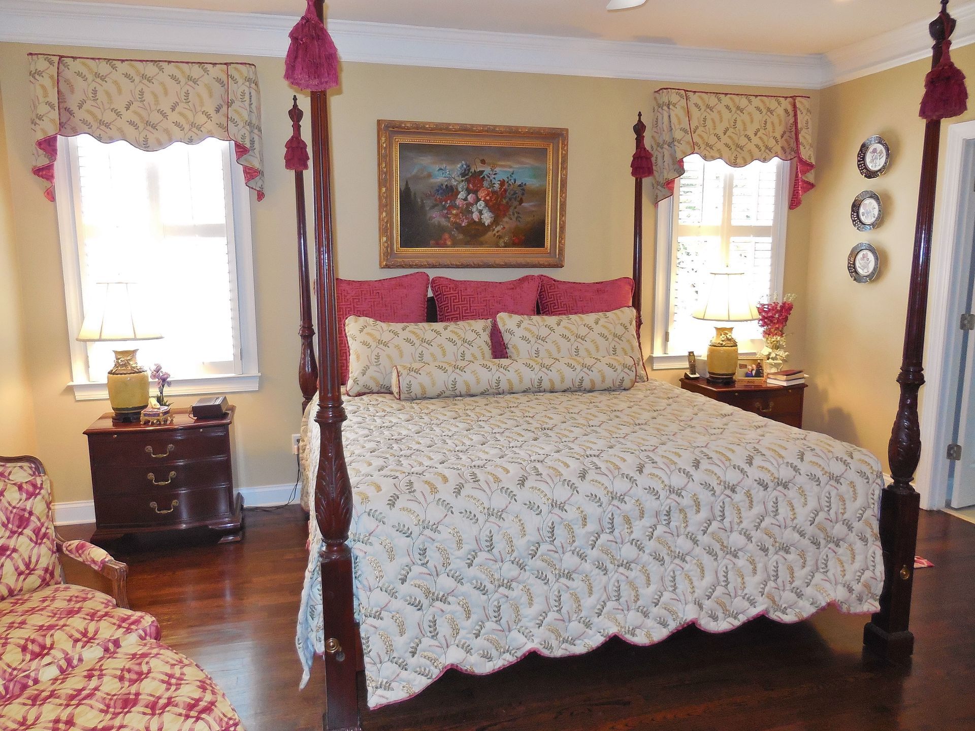 Cozy bedroom with four-poster bed, pink accents, floral bedding, and windows on either side