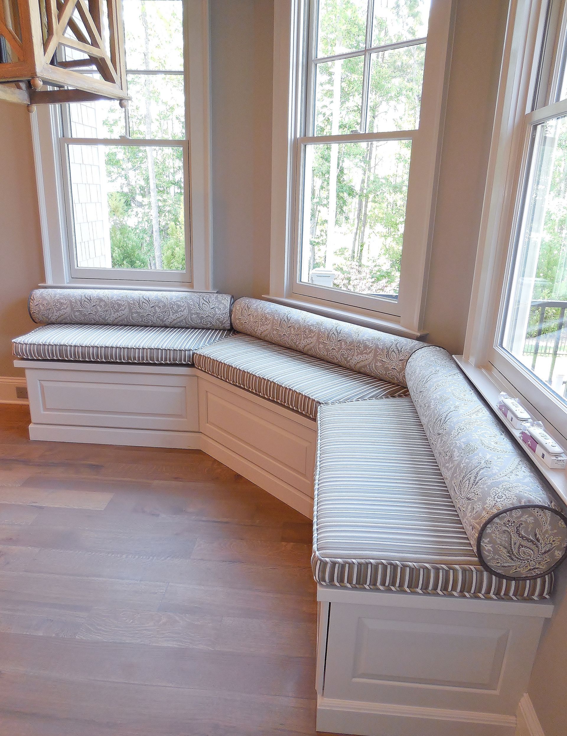 Curved window seat with white cabinets and patterned cushions in a bright room with large windows