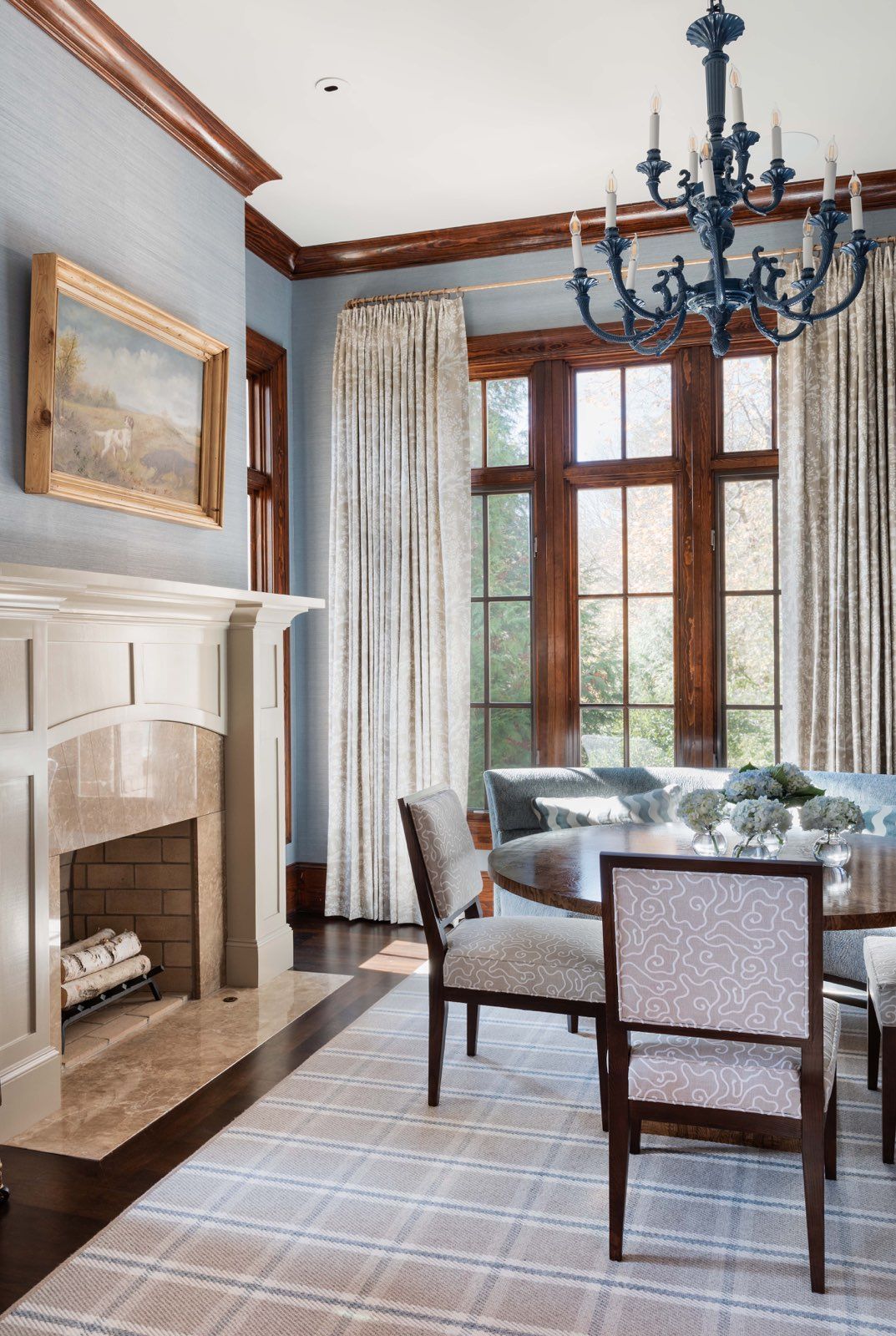 Elegant dining room with fireplace, chandelier, large windows, and a table with patterned chairs and curtains