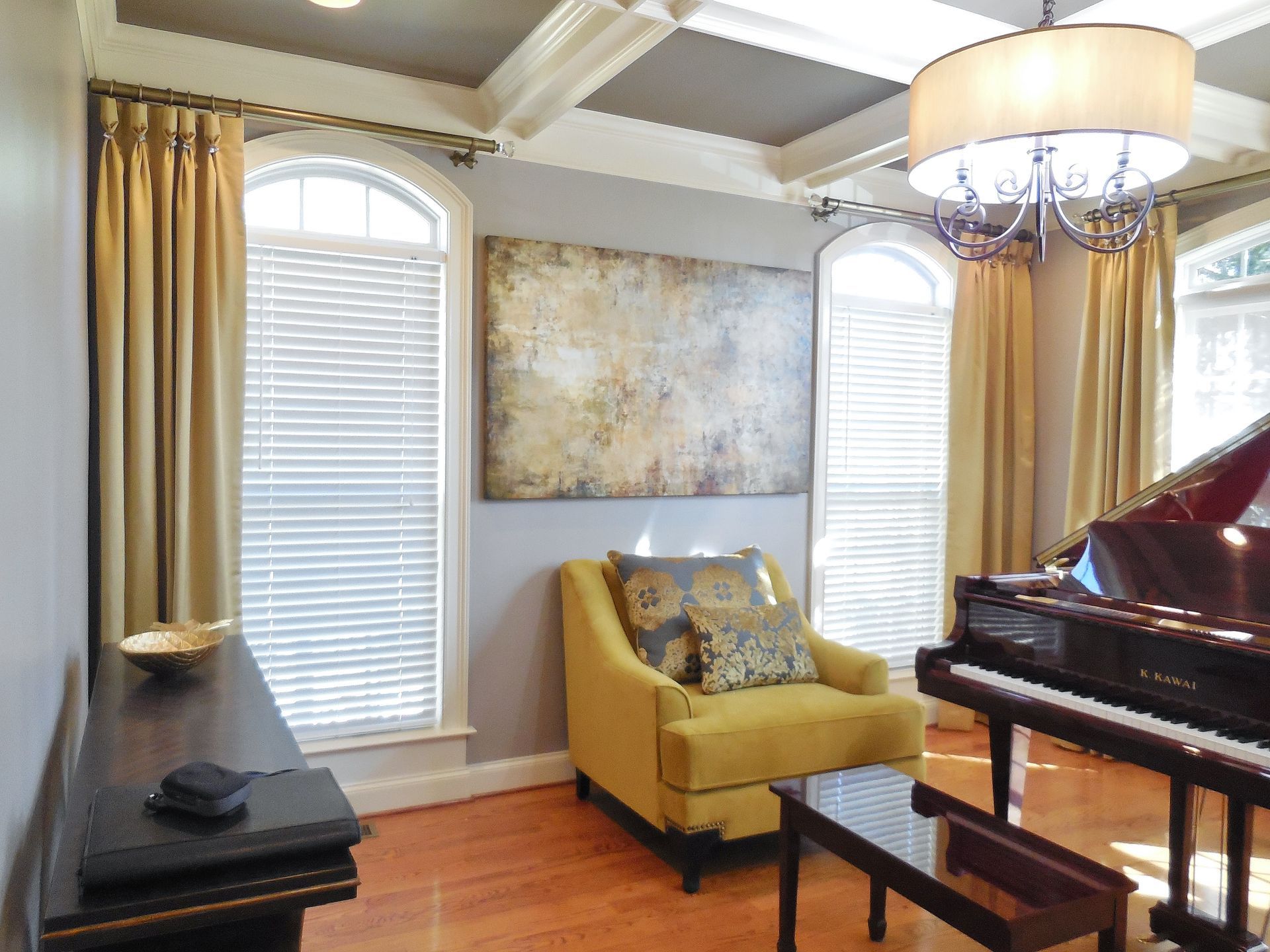 Elegant living room with piano, yellow chair, chandelier, and arched windows with blinds