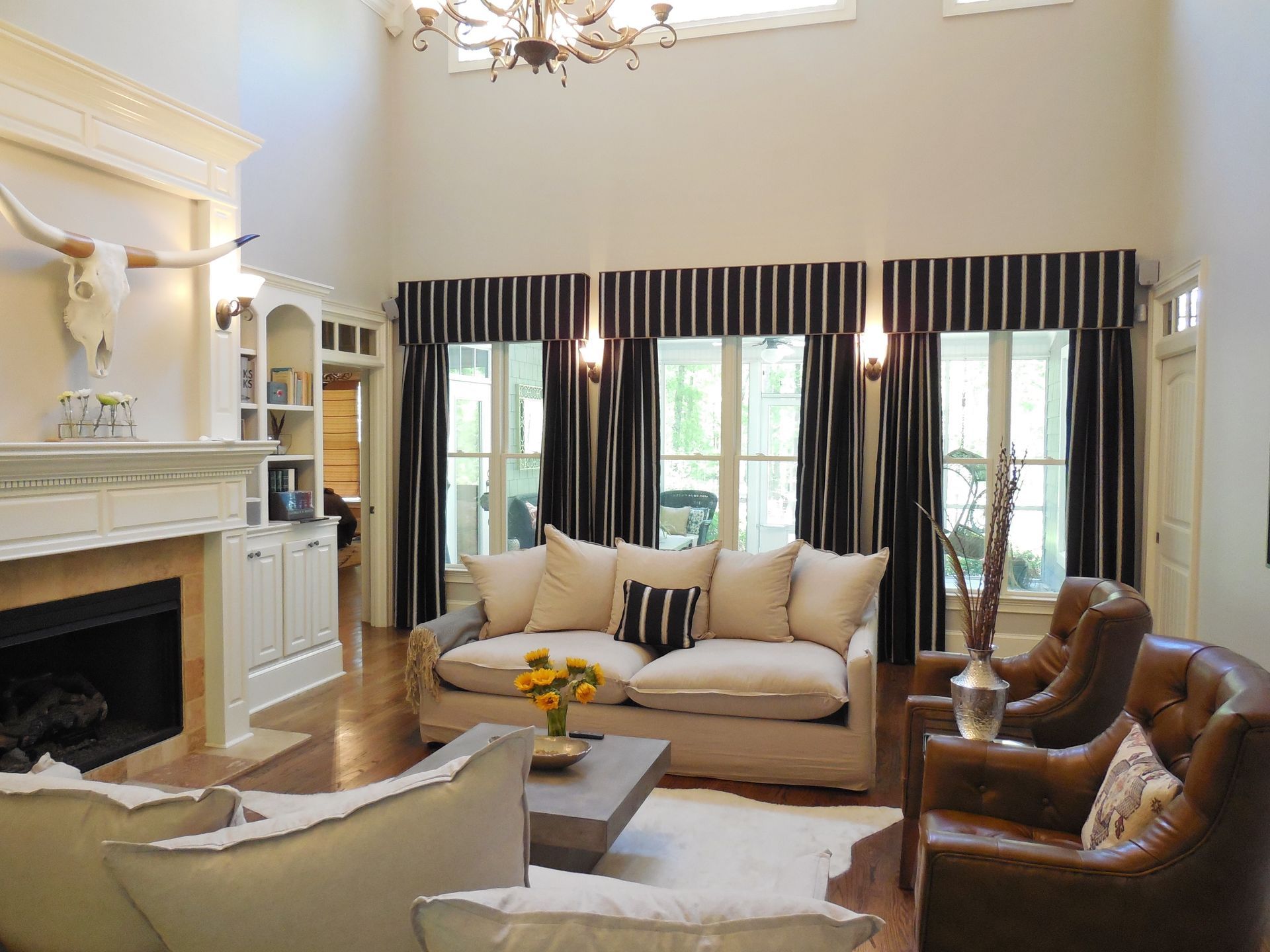 Elegant living room with fireplace, beige sofas, brown chairs, and tall dark curtains over large windows