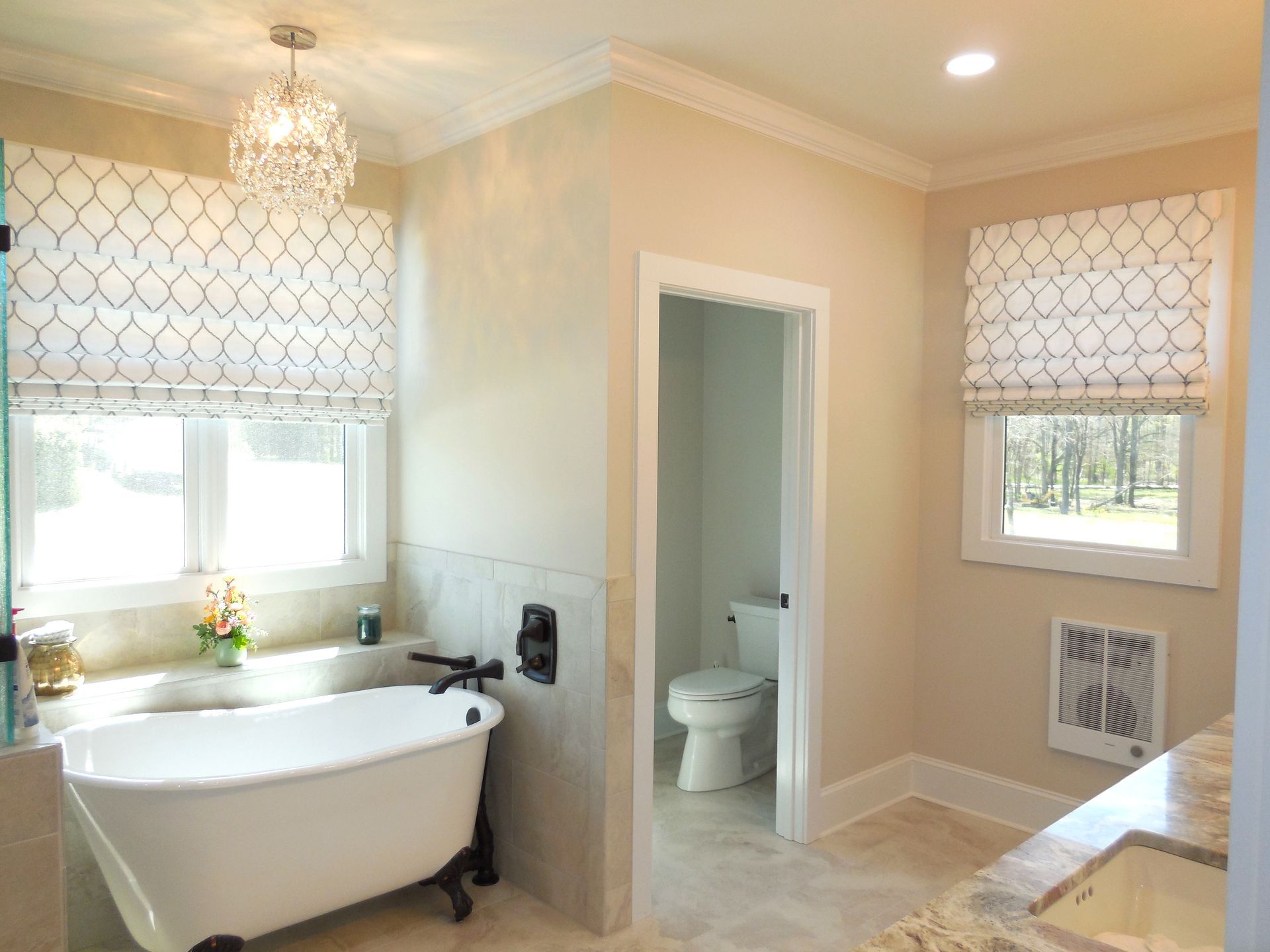 Bright bathroom with freestanding tub, double windows, marble tile, and a small toilet room.