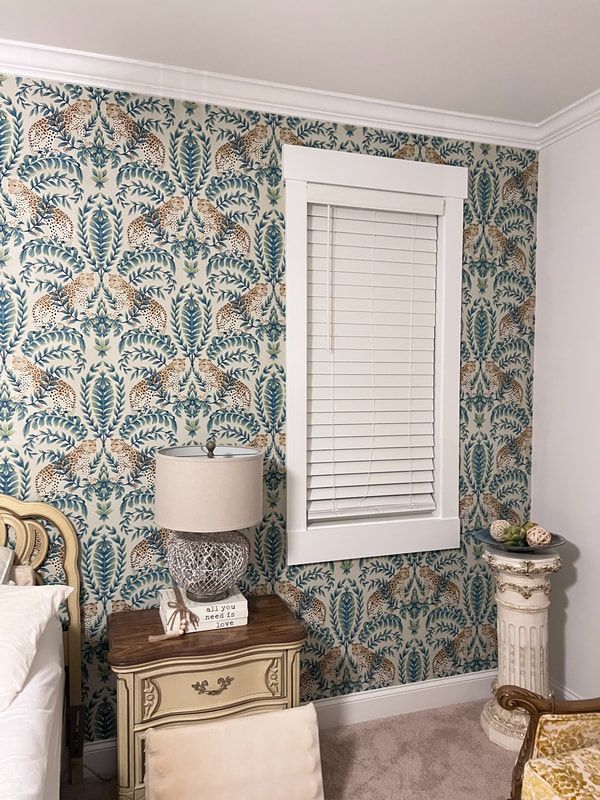 Bedroom corner with teal floral wallpaper, white window blind, nightstand lamp, and small pedestal table