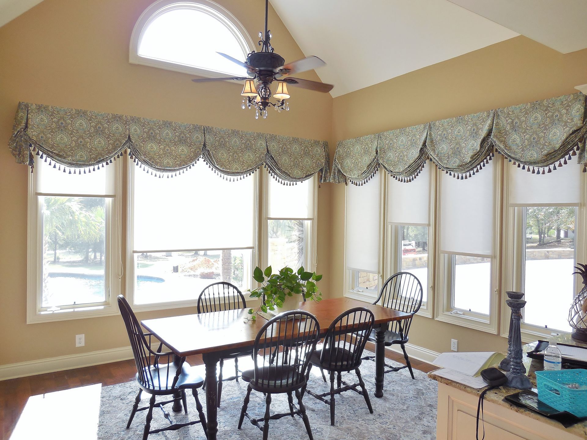 Bright dining room with large windows, patterned valances, and a table surrounded by chairs
