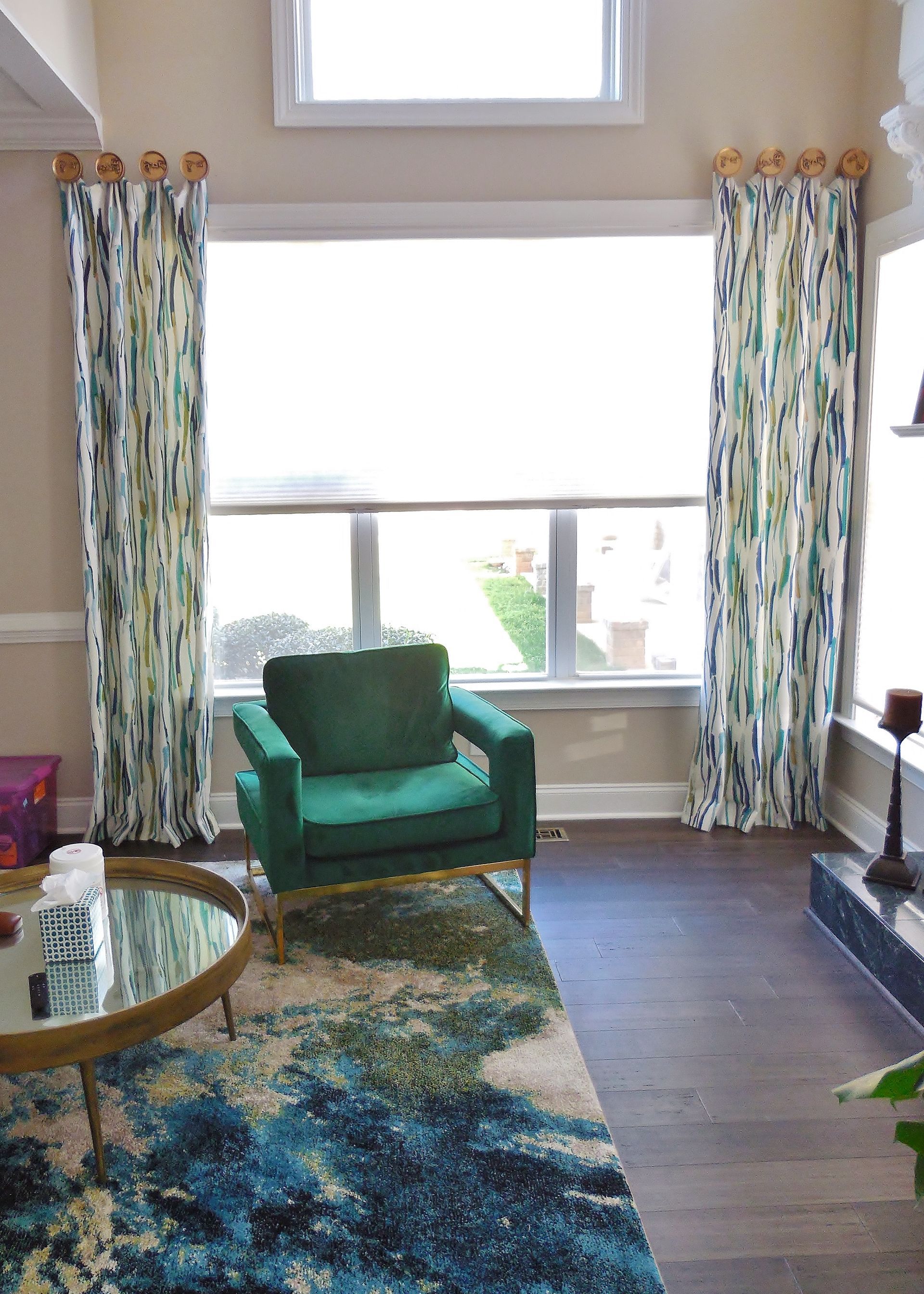 Bright living room with teal chair, patterned rug, and tall windows with curtains