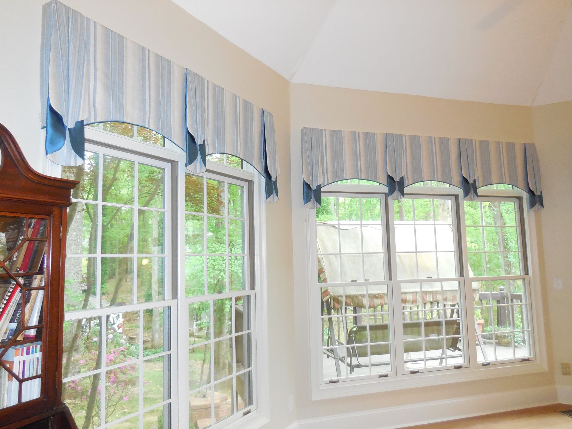 Bright room with large white-trimmed windows and blue-and-white valances overlooking greenery outside