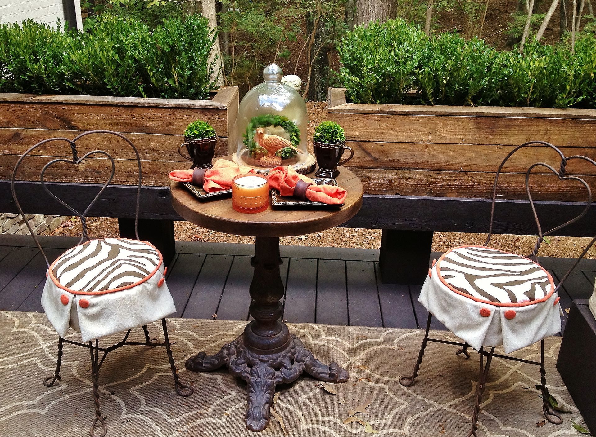 Outdoor patio table set with fall decor, orange candles, and two white patterned chairs on a rug.