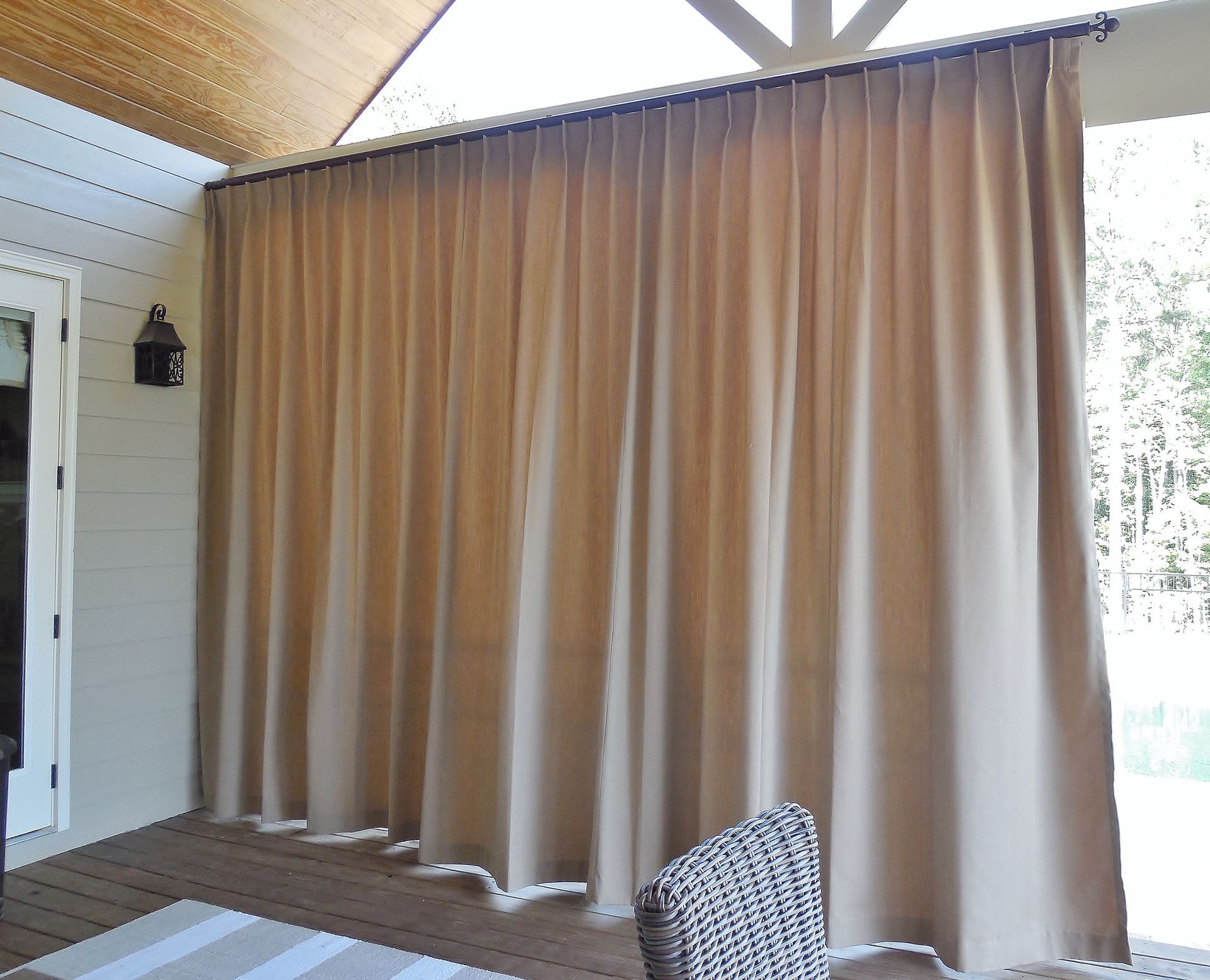 Outdoor patio with large beige curtains and a striped chair in the corner.