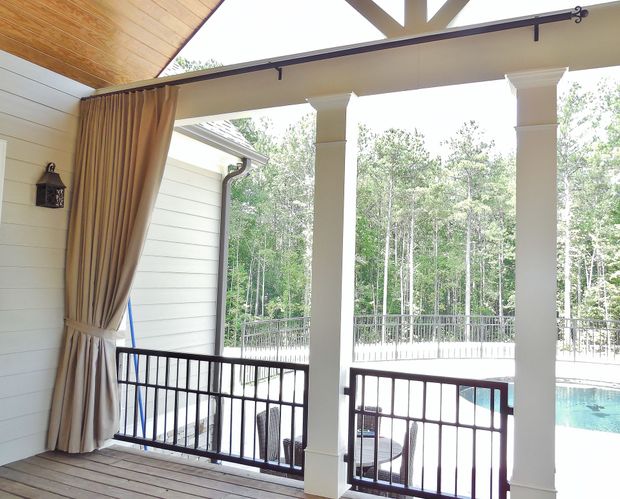 Covered patio with white columns, railing, and curtains overlooking a pool and trees