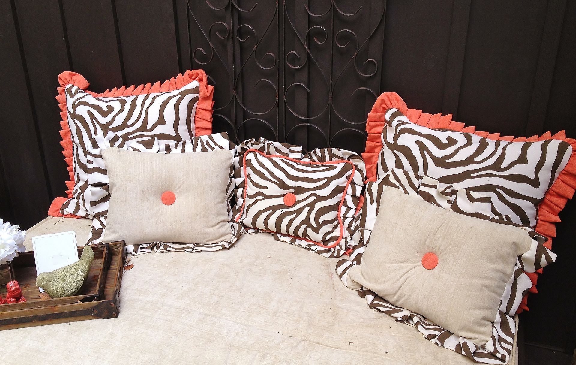 Four zebra-print and beige throw pillows with orange accents on a light couch against a dark wall