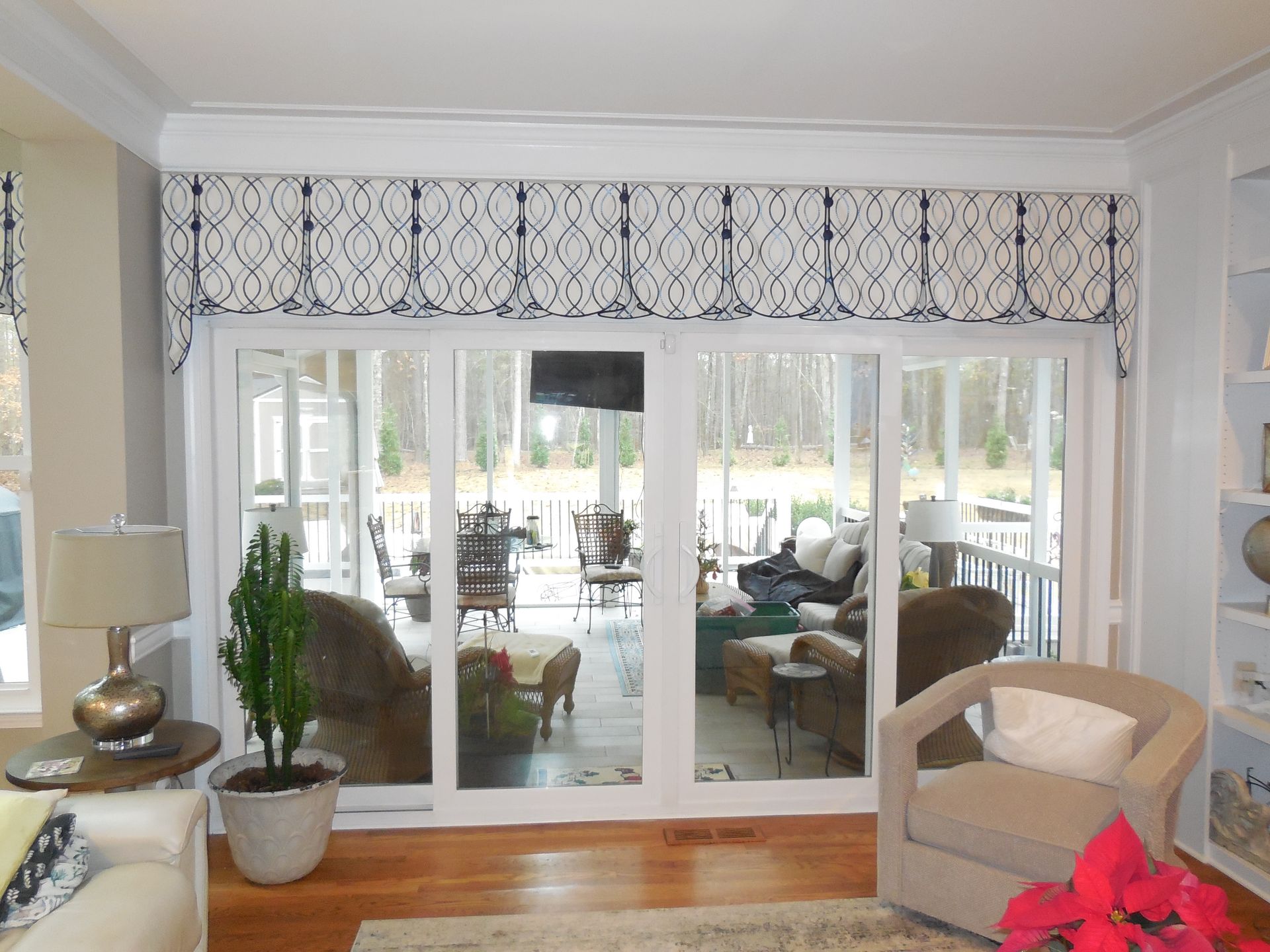 Bright living room with sliding glass doors, patterned valance, beige chair, and potted plant.