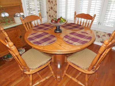 Round wooden dining table with four chairs, purple placemats, and a fruit bowl in a bright breakfast nook