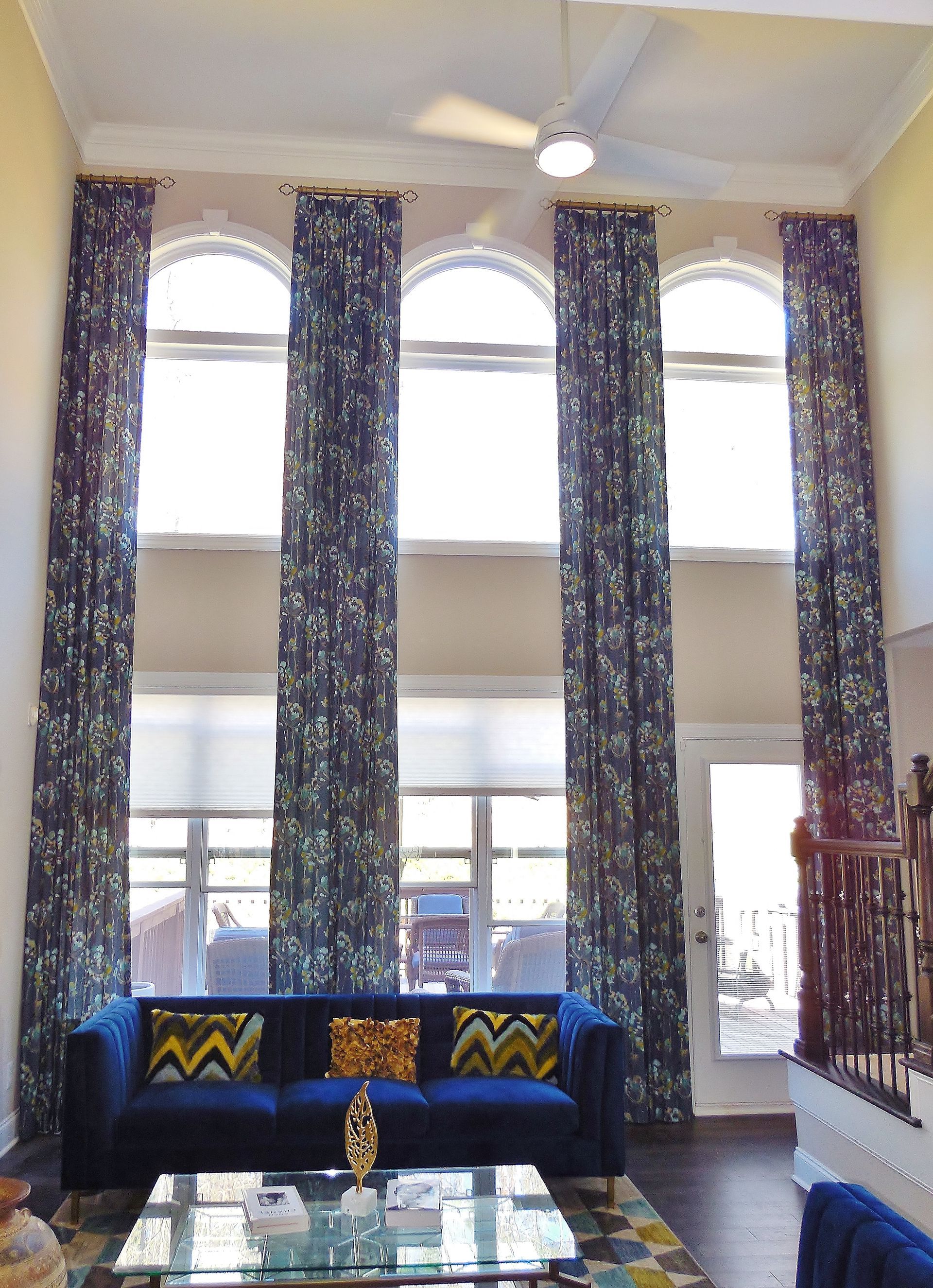 Bright living room with tall arched windows, patterned curtains, blue sofa, and glass coffee table