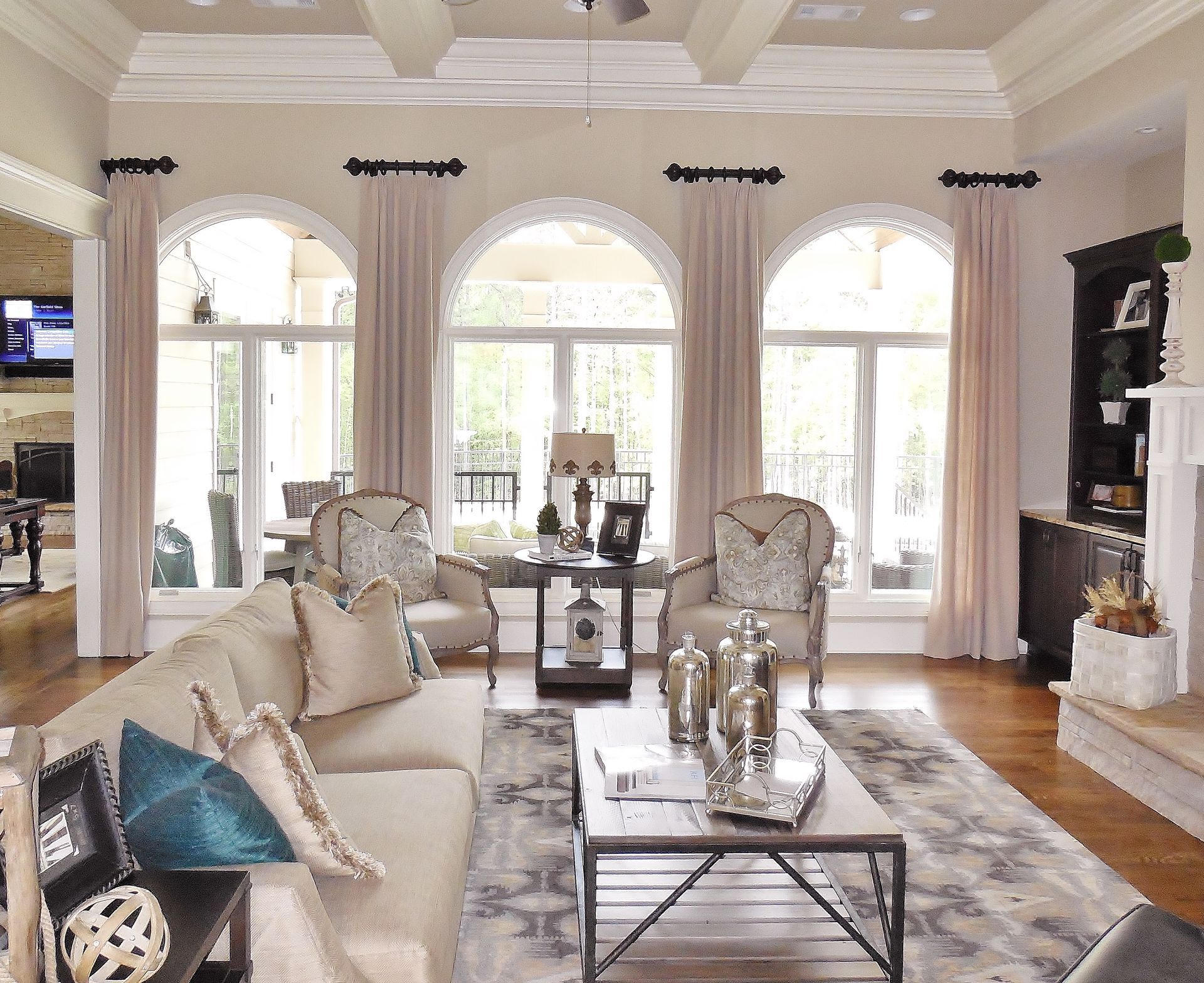 Elegant living room with beige sofas, arched windows, hardwood floors, and a glass coffee table.