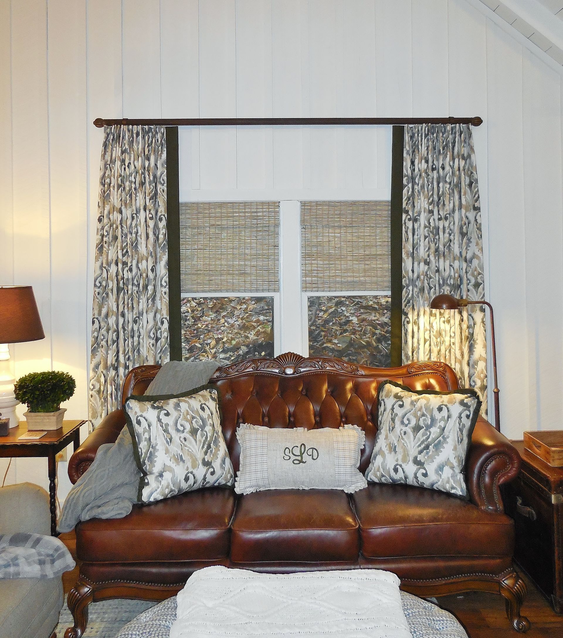 Brown leather sofa in a cozy living room with patterned curtains and a window behind it