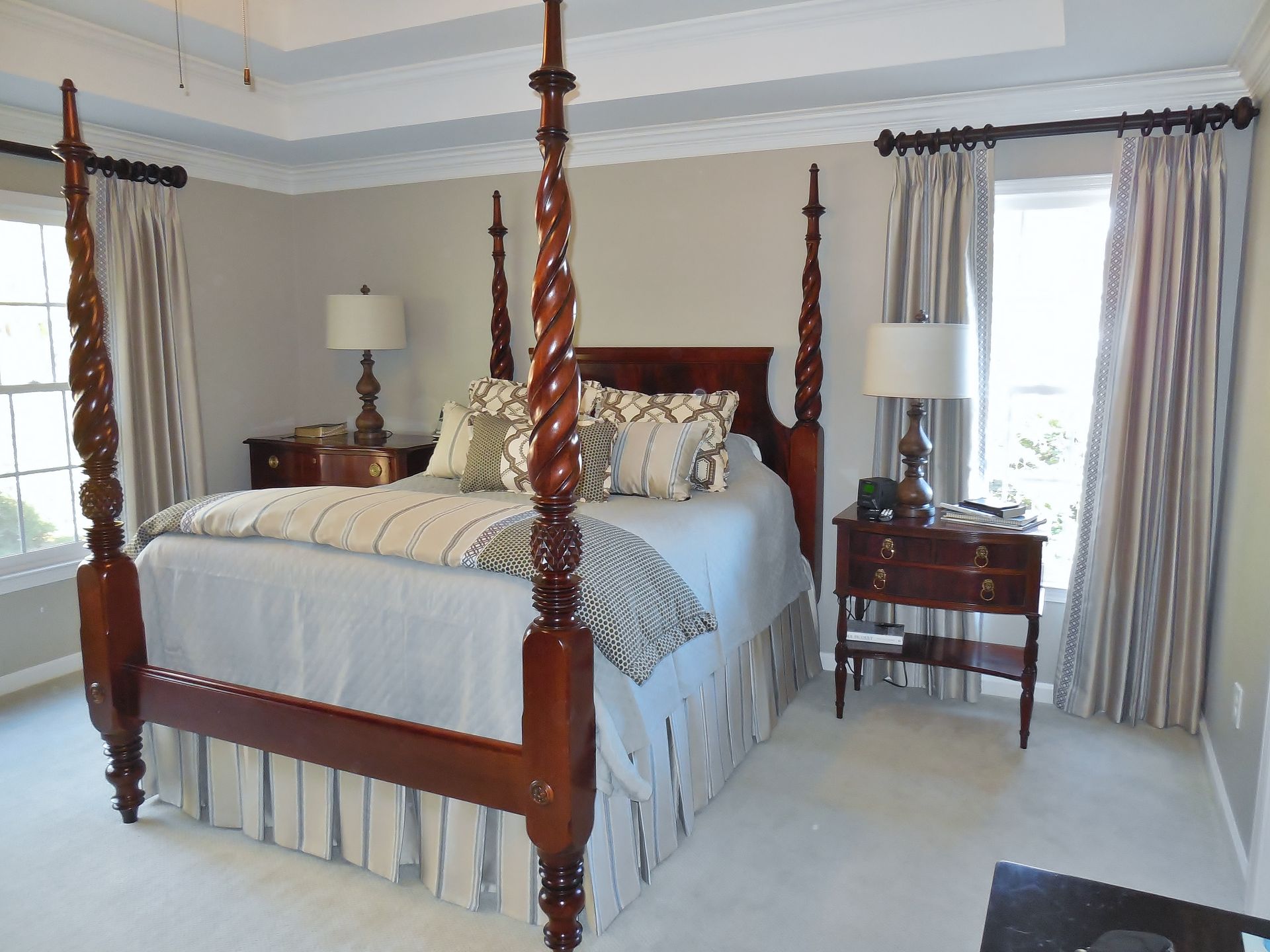 Elegant bedroom with a four-poster bed, bedside tables, lamps, and sheer curtains beside a window.