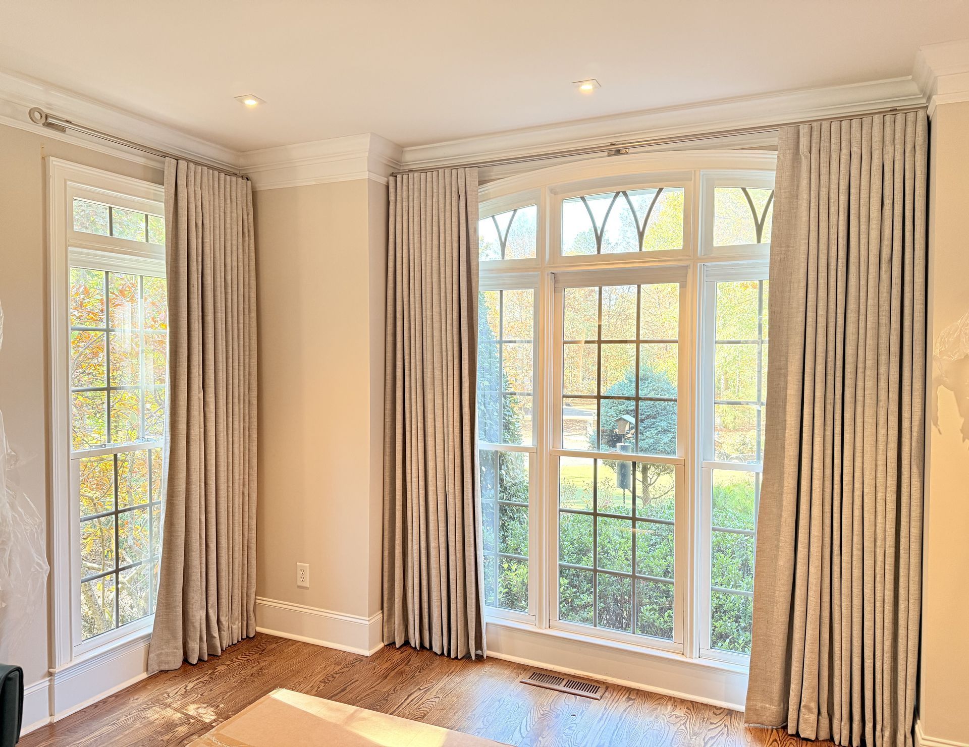 Bright empty room with large windows, beige curtains, and sunlight on wood floors