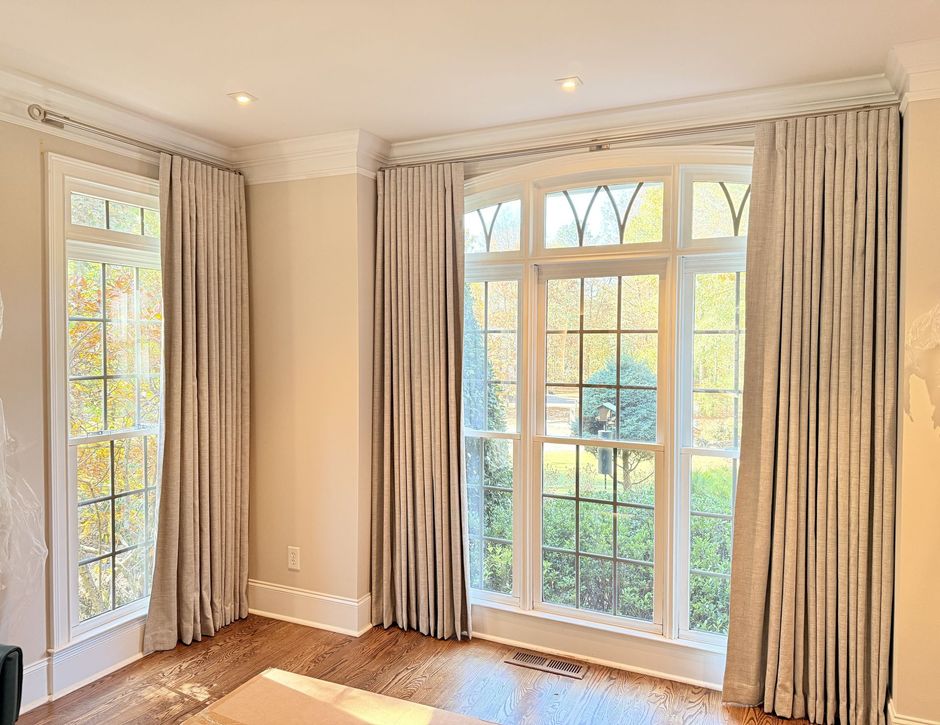 Bright empty room with beige curtains and large windows letting in sunlight over a wooden floor