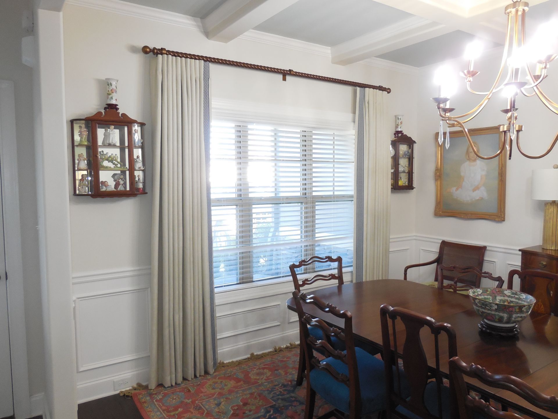 Formal dining room with white walls, wooden table, chairs, chandelier, and large window with curtains