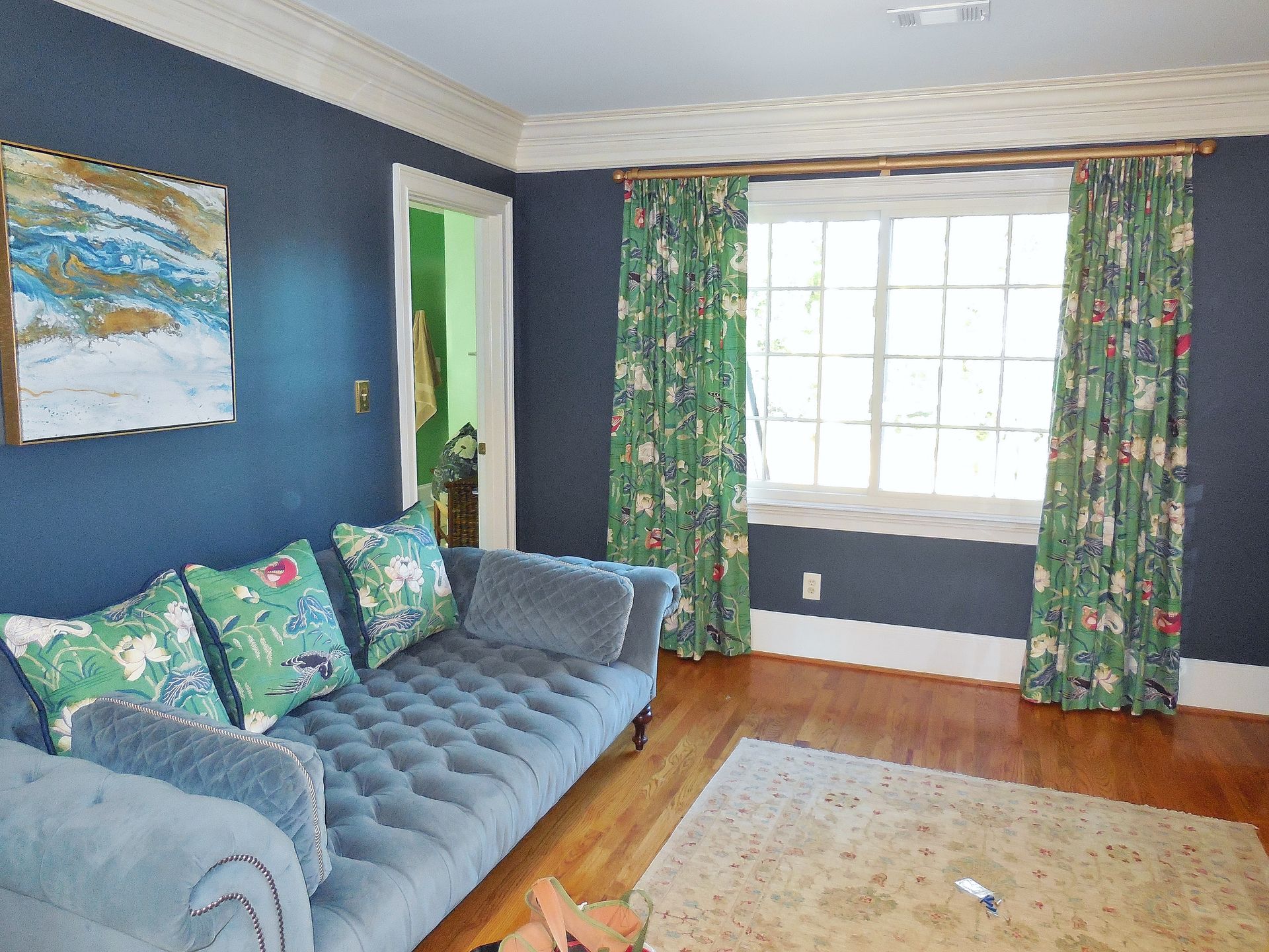 Cozy living room with blue sofa, patterned curtains, dark walls, and sunlight from a large window