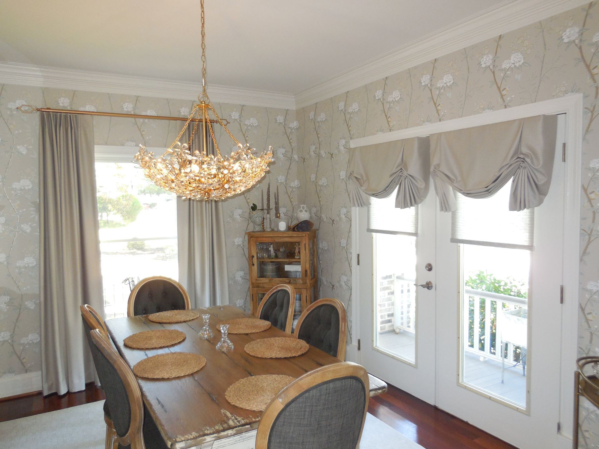 Elegant dining room with chandelier, oval table, upholstered chairs, and French doors with valances