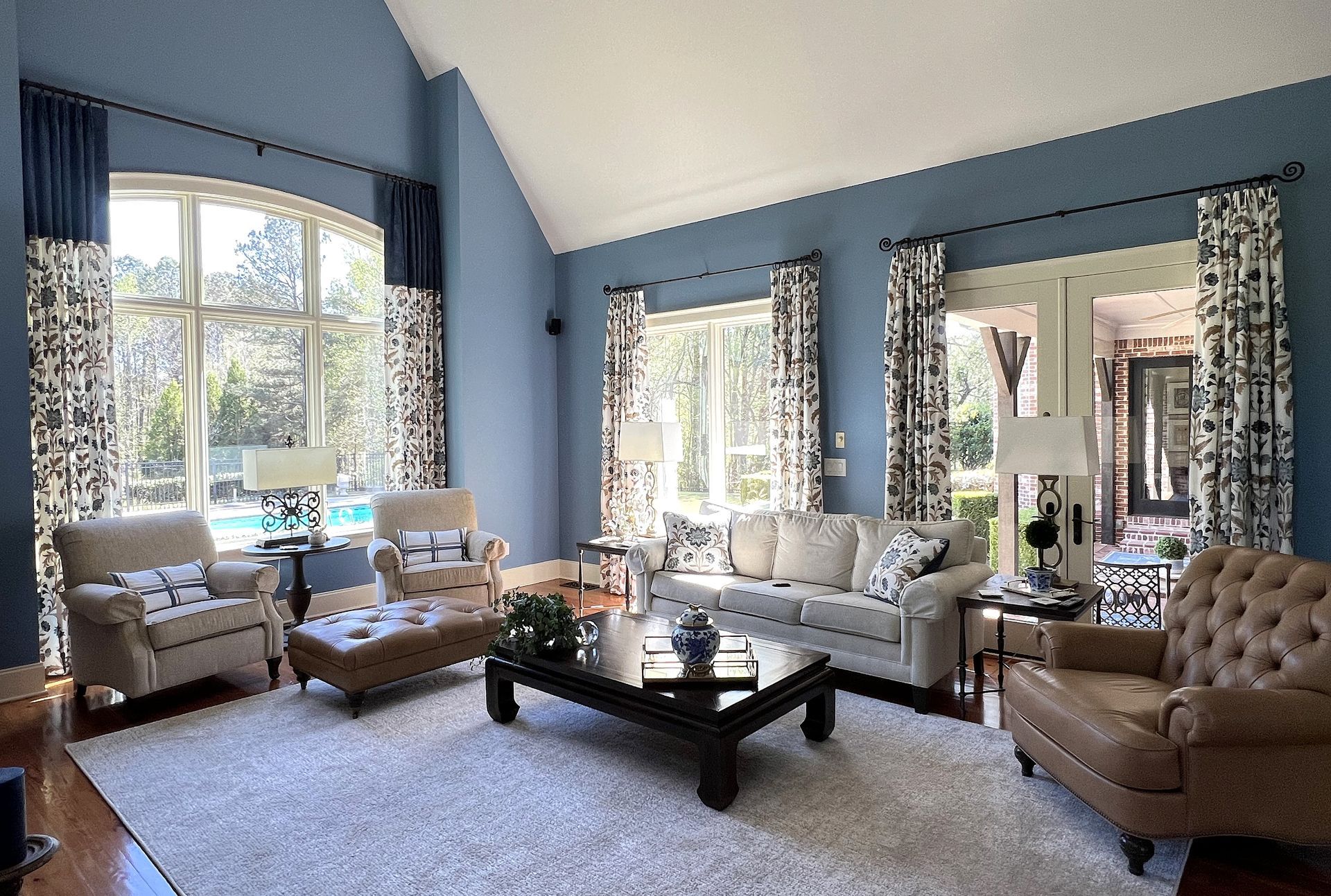 Bright living room with blue walls, large windows, and beige sofas around a black coffee table.