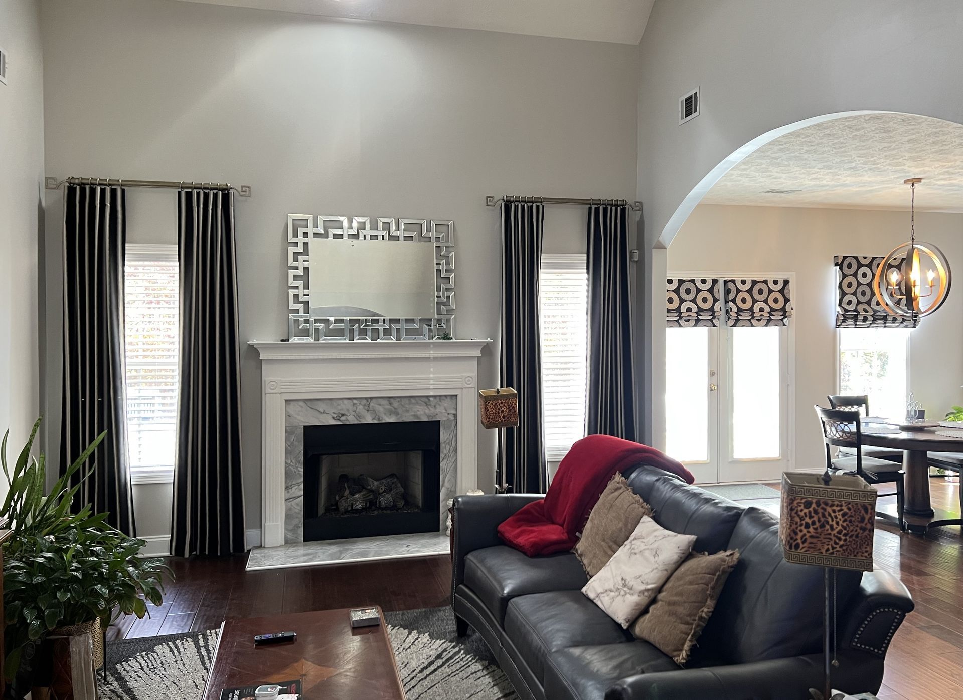 Living room with fireplace, striped curtains, black sofa, and arched pass-through to kitchen.