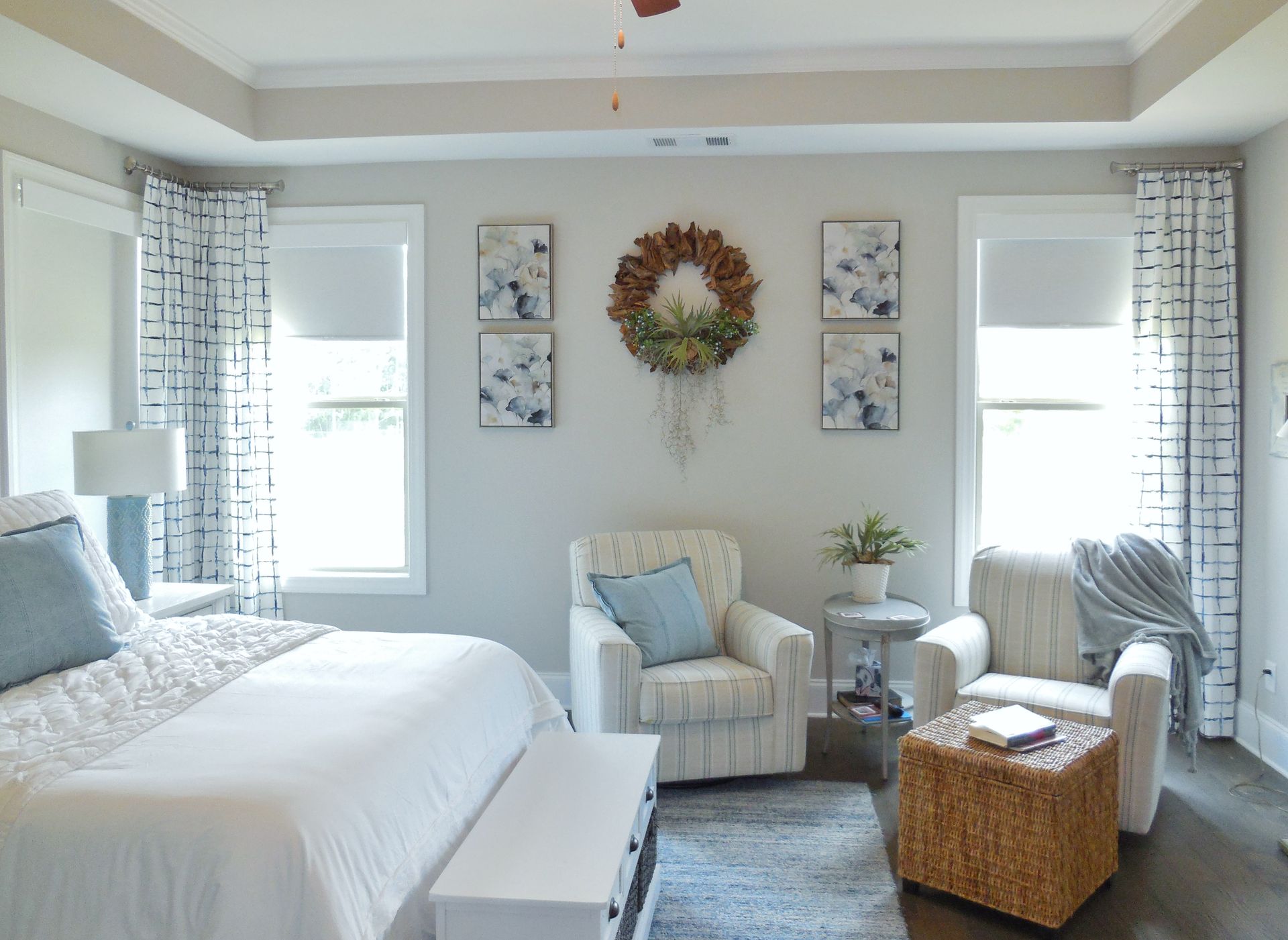 Bright airy bedroom with white bed, armchair, wreath wall art, and wicker storage basket