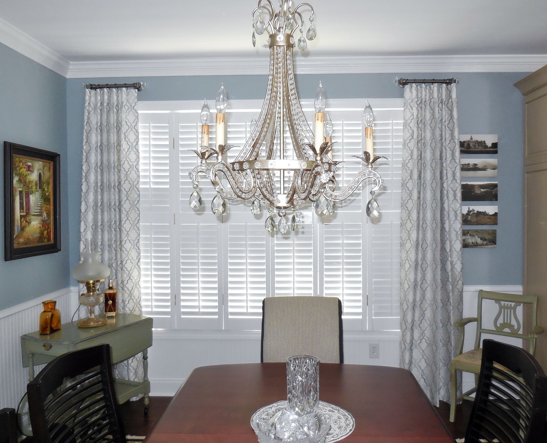 Elegant dining room with crystal chandelier, blue walls, white shutters, and dark wood table