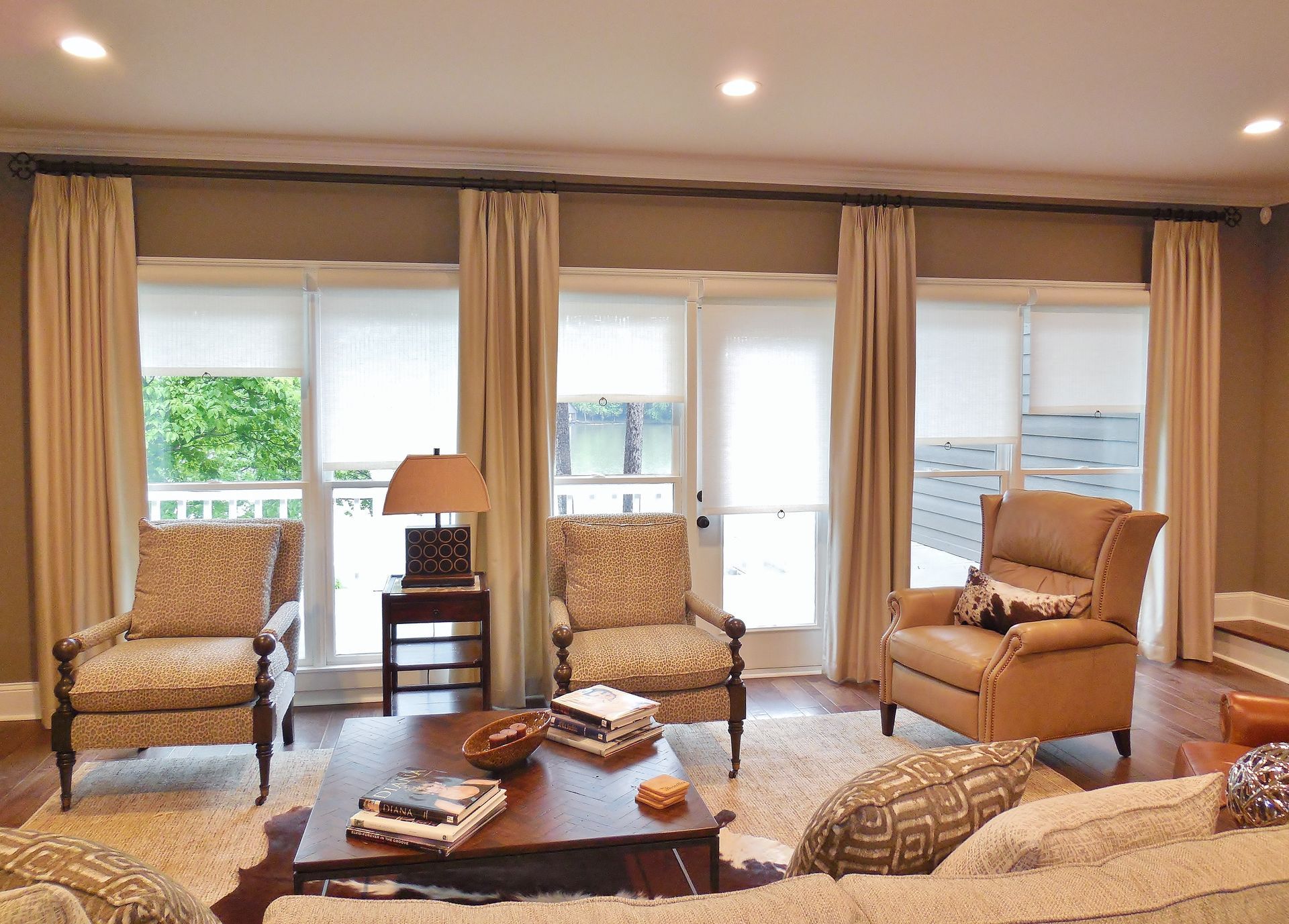 Bright living room with beige armchairs, coffee table, and large windows with curtains.