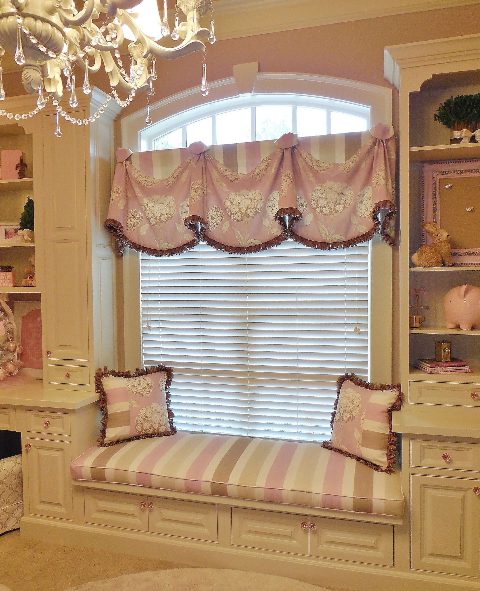 Elegant bay window seat with pink striped cushions and draped valance in a cream room
