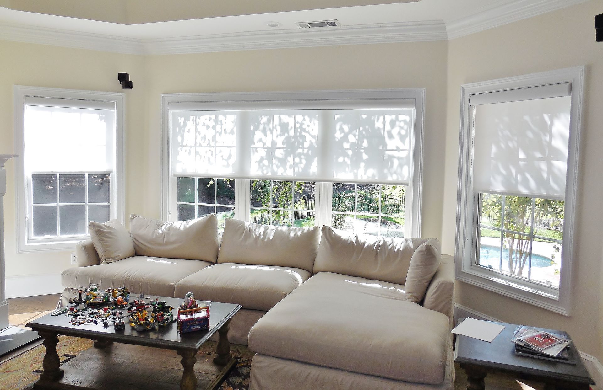 Bright living room with beige sectional, coffee table, and large windows overlooking a pool