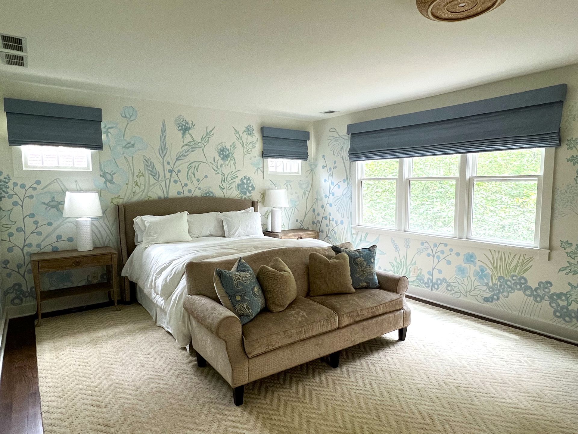 Bright bedroom with a bed, sofa at its foot, blue wallpaper, and large windows with blinds