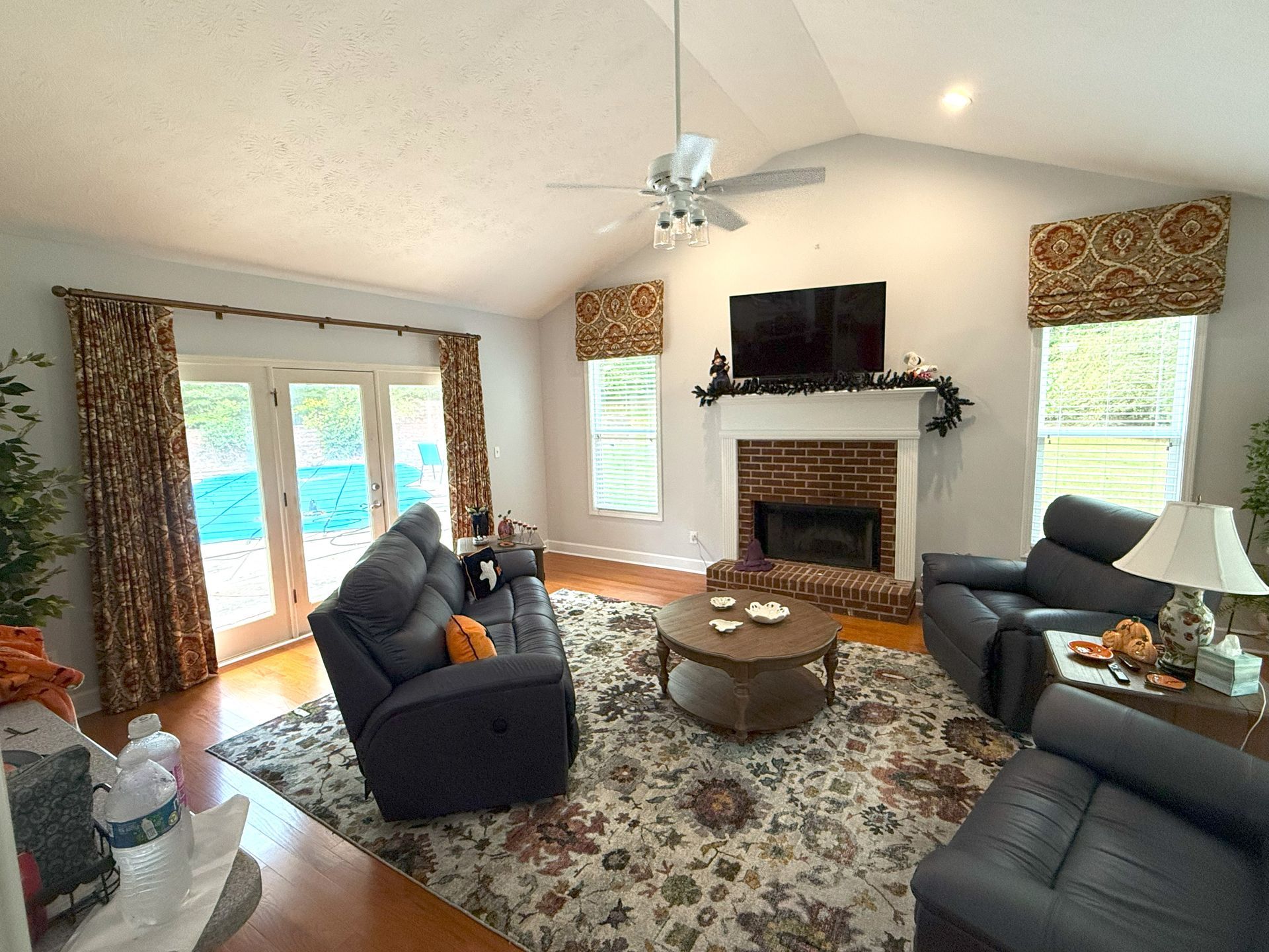 Bright living room with fireplace, TV, patterned rug, and large windows with curtains