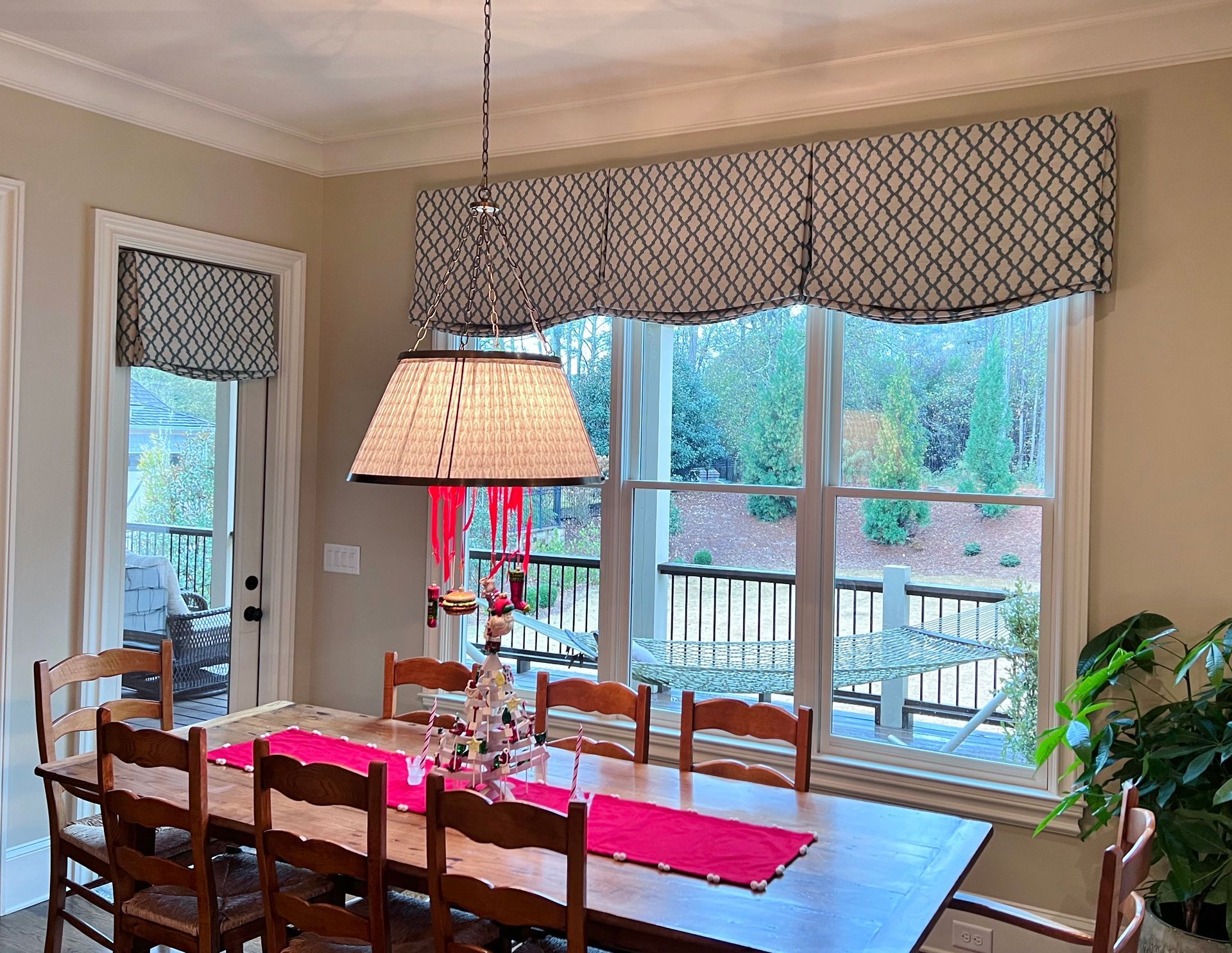 Dining room with wooden table, red runner, and window seat overlooking a deck and trees