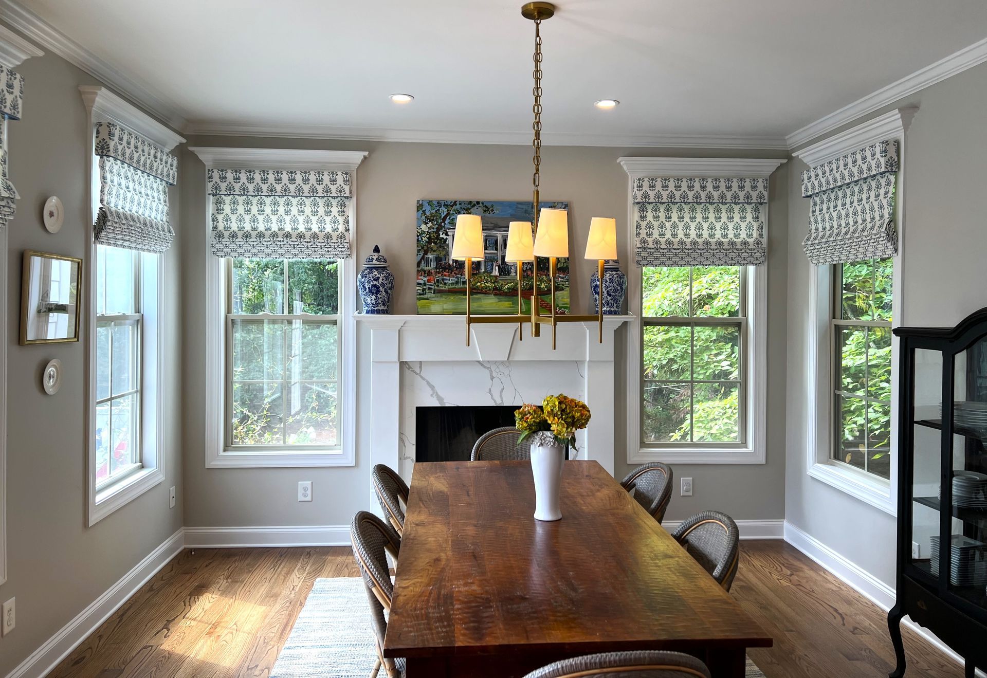 Dining room with long wooden table, chandelier, fireplace, and patterned window treatments.